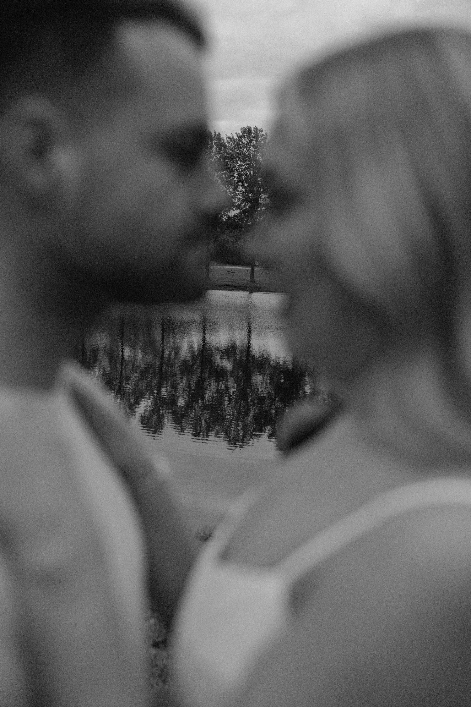 An artistic black and white portrait captures a couple's intimate moment with nature reflected between them.