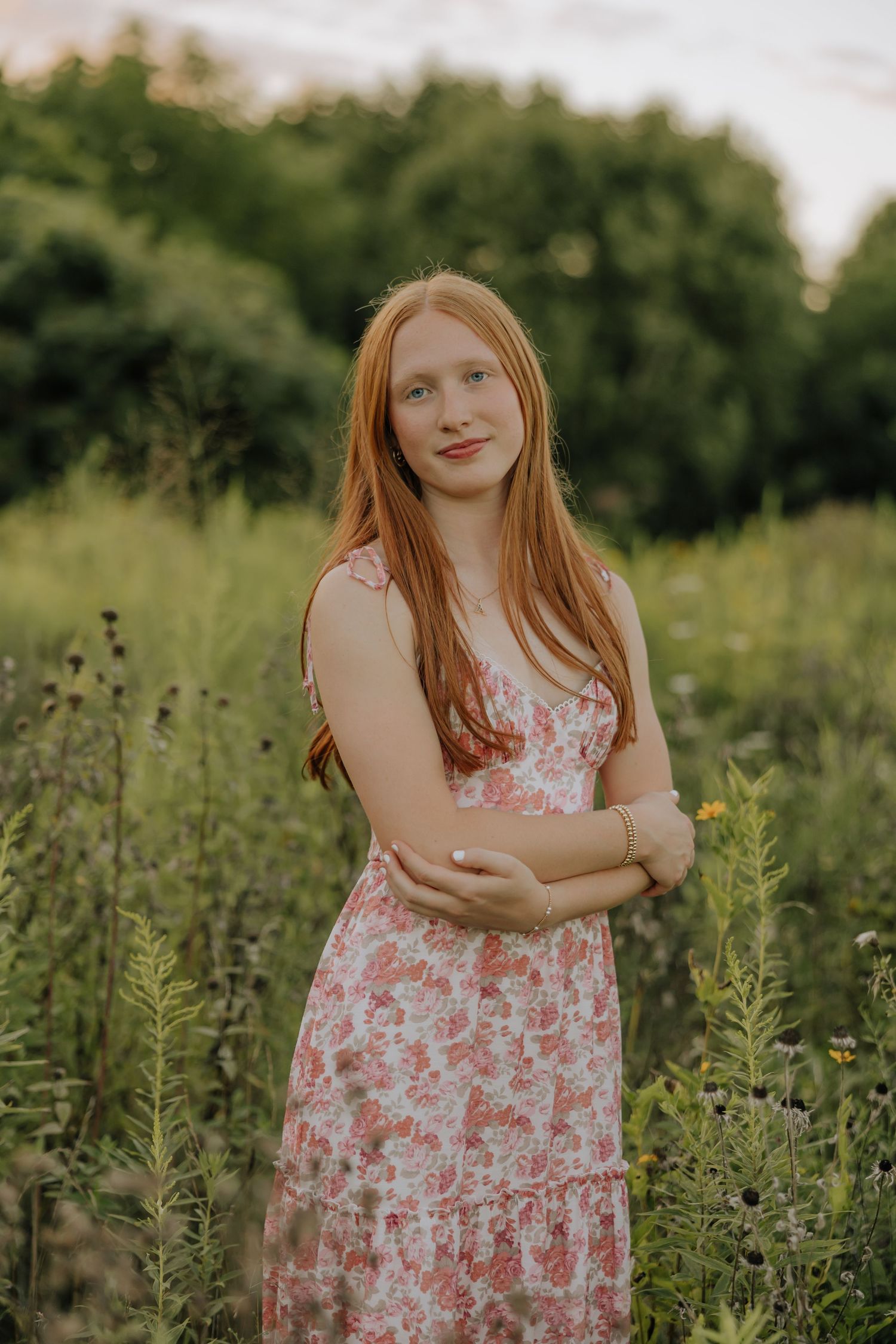 A person in a floral summer dress stands in a lush green meadow during golden hour.