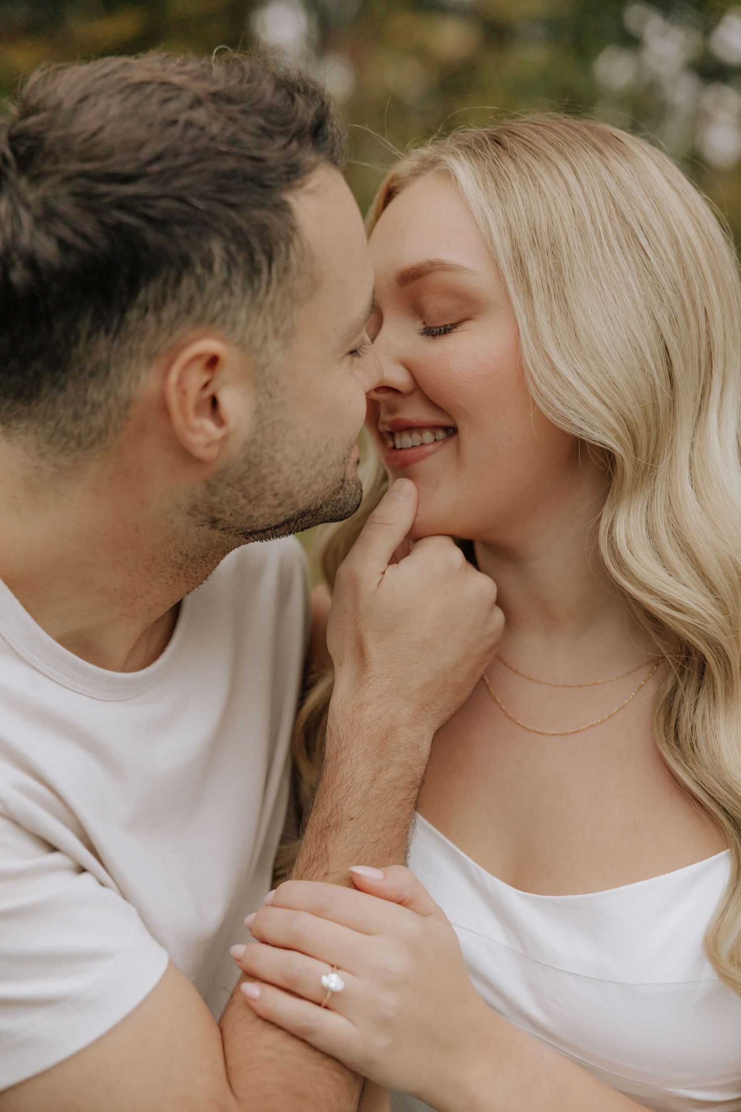 A romantic couple in white shirts share an intimate moment with gentle smiles and tender touch.