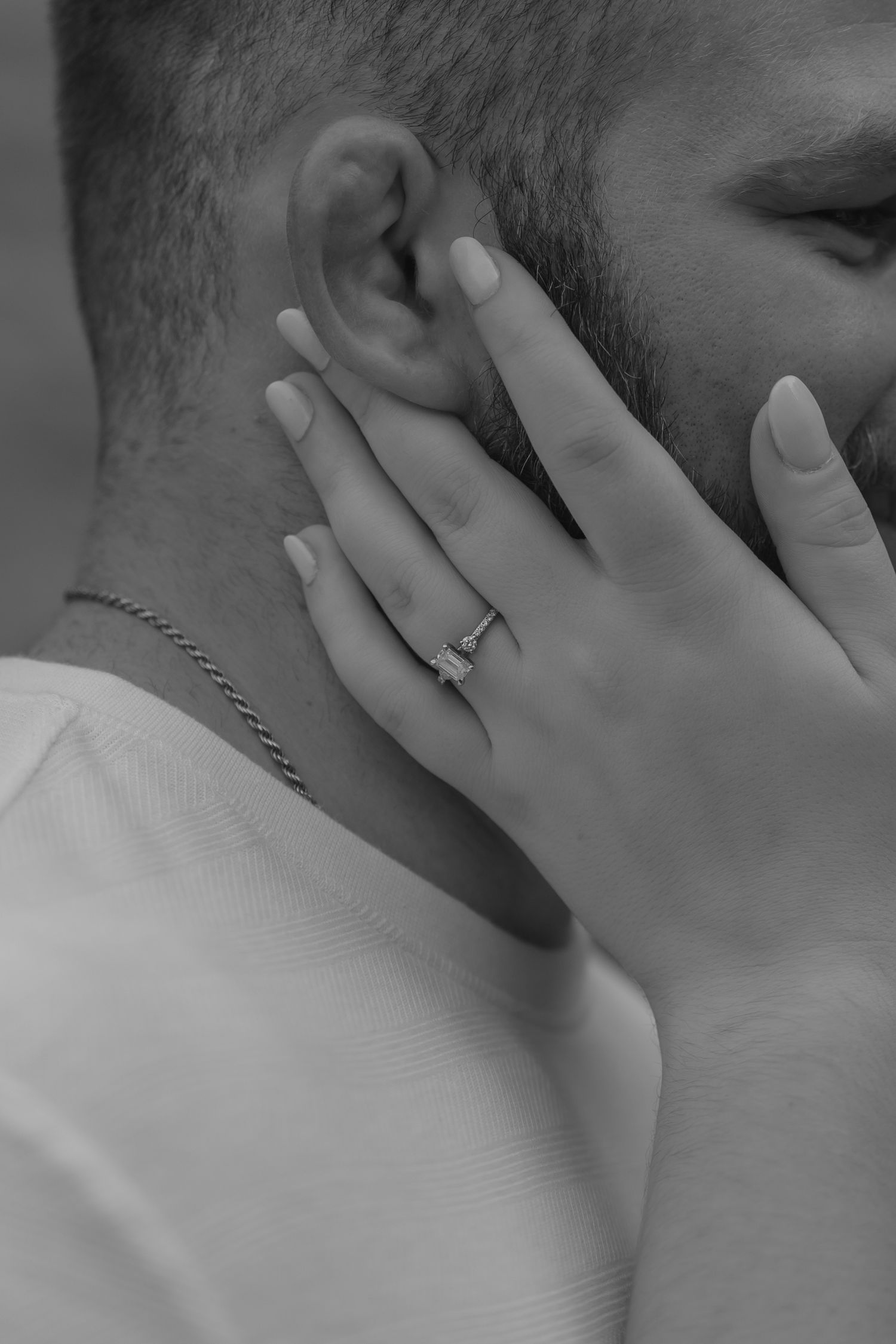 Black and white photo of a woman's hand with an engagement ring resting on a man's face.
