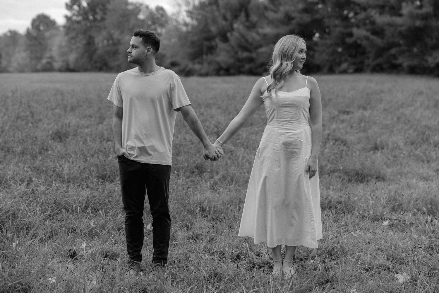 A couple in wedding attire holds hands while walking through a grassy meadow in black and white photography.