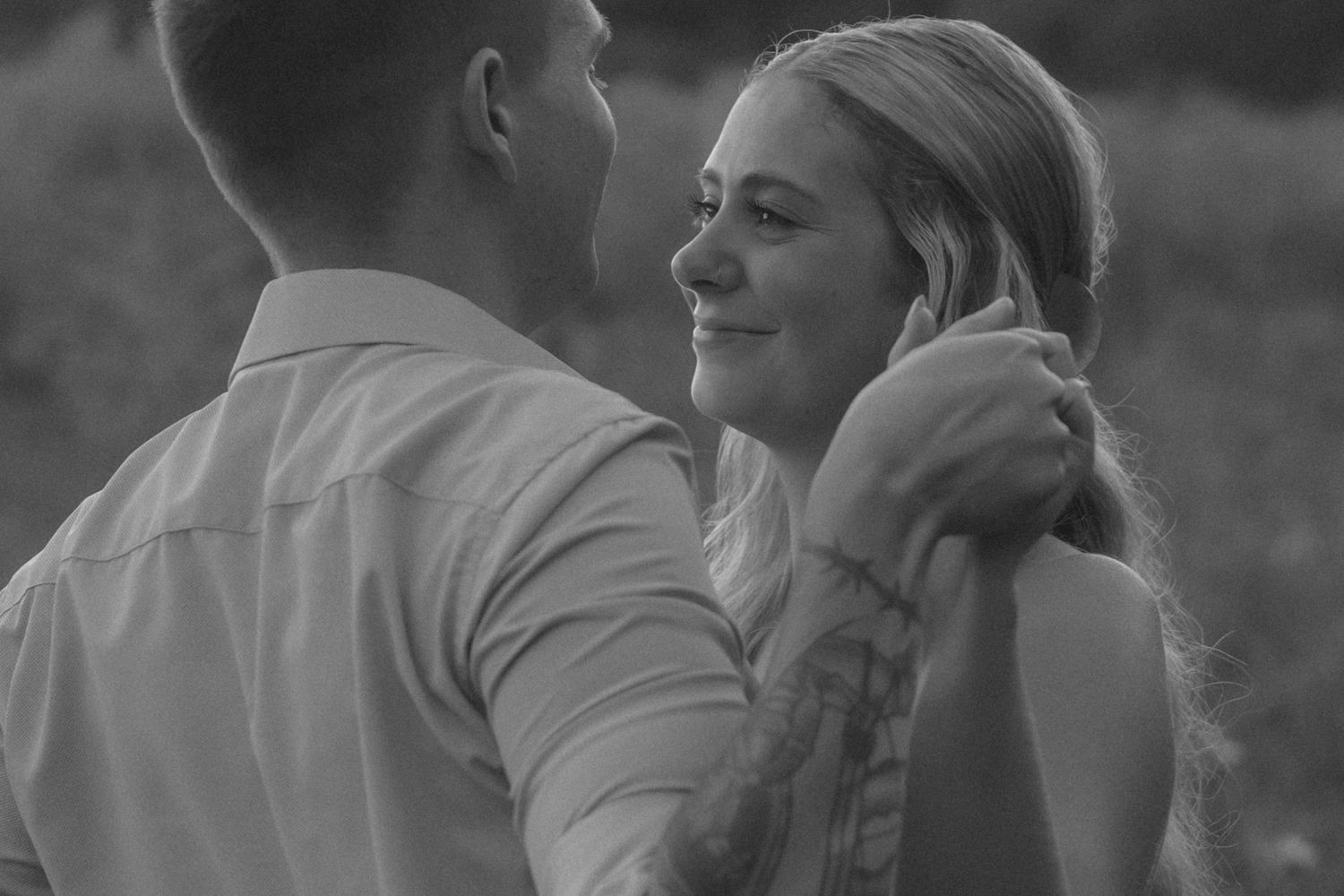 Black and white photo of a couple sharing a tender moment, man holding woman's face as she smiles warmly.