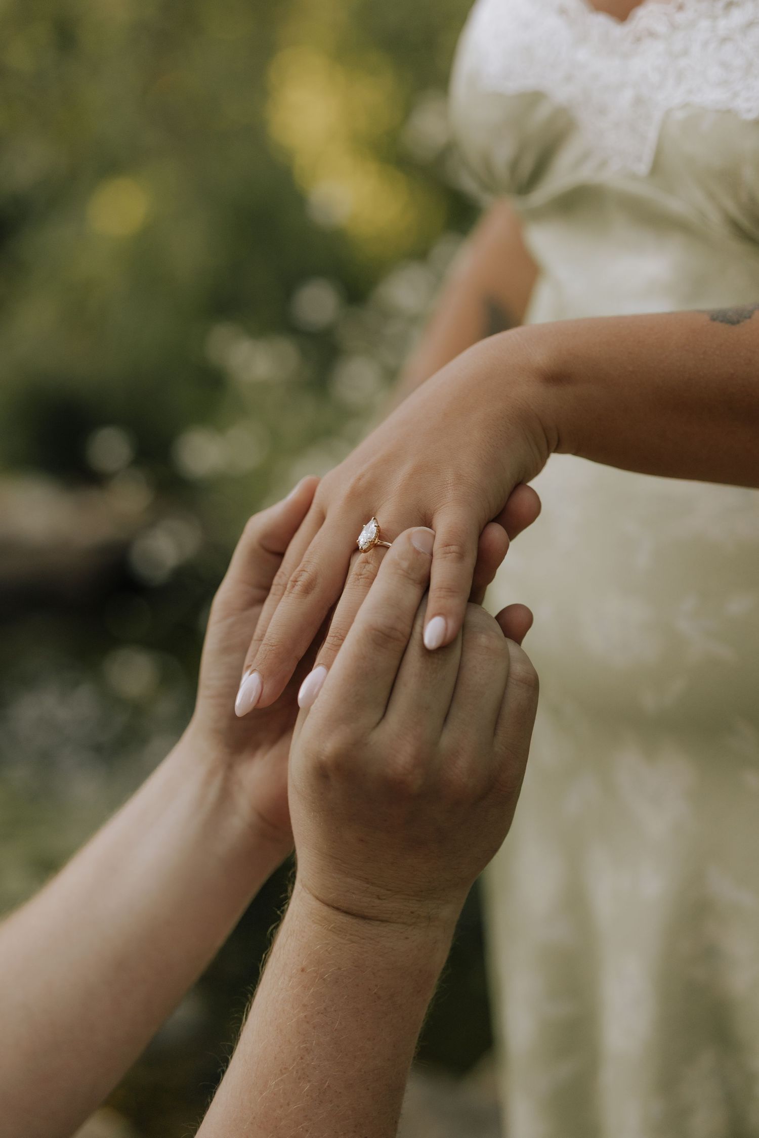 Close-up of a bride receiving a diamond engagement ring on her finger during an outdoor wedding ceremony.