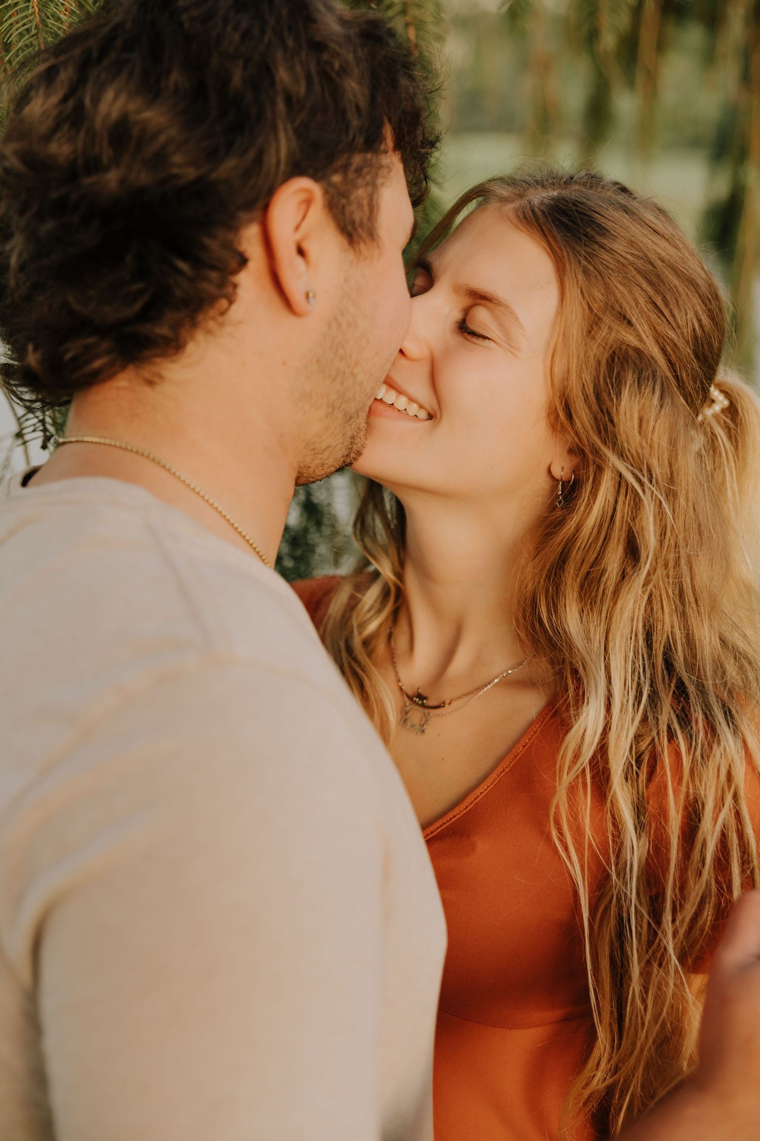 A romantic couple sharing intimate kisses in warm golden sunlight against a natural outdoor background.