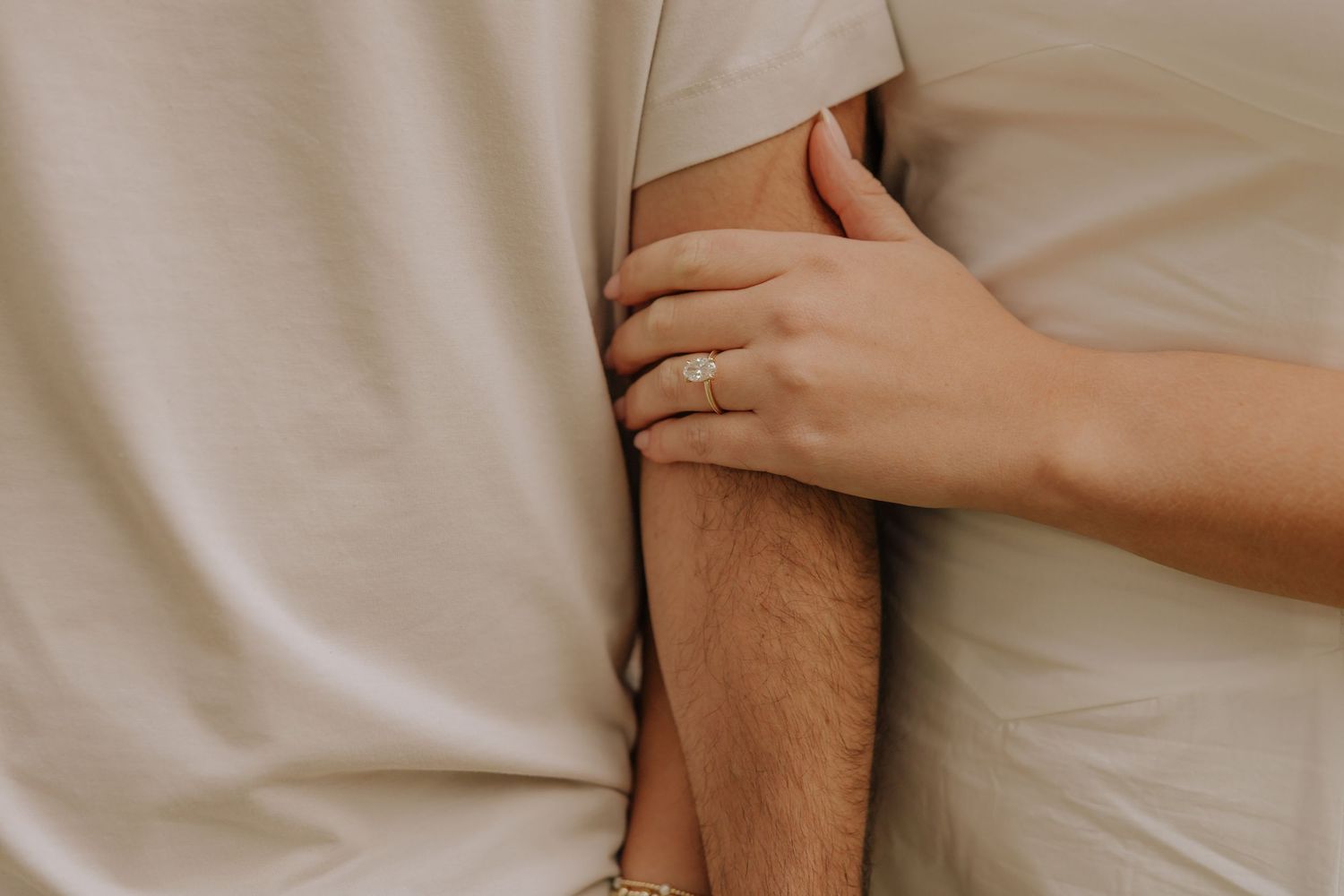 Two people hold hands intimately against a neutral beige background showing connection and tenderness.