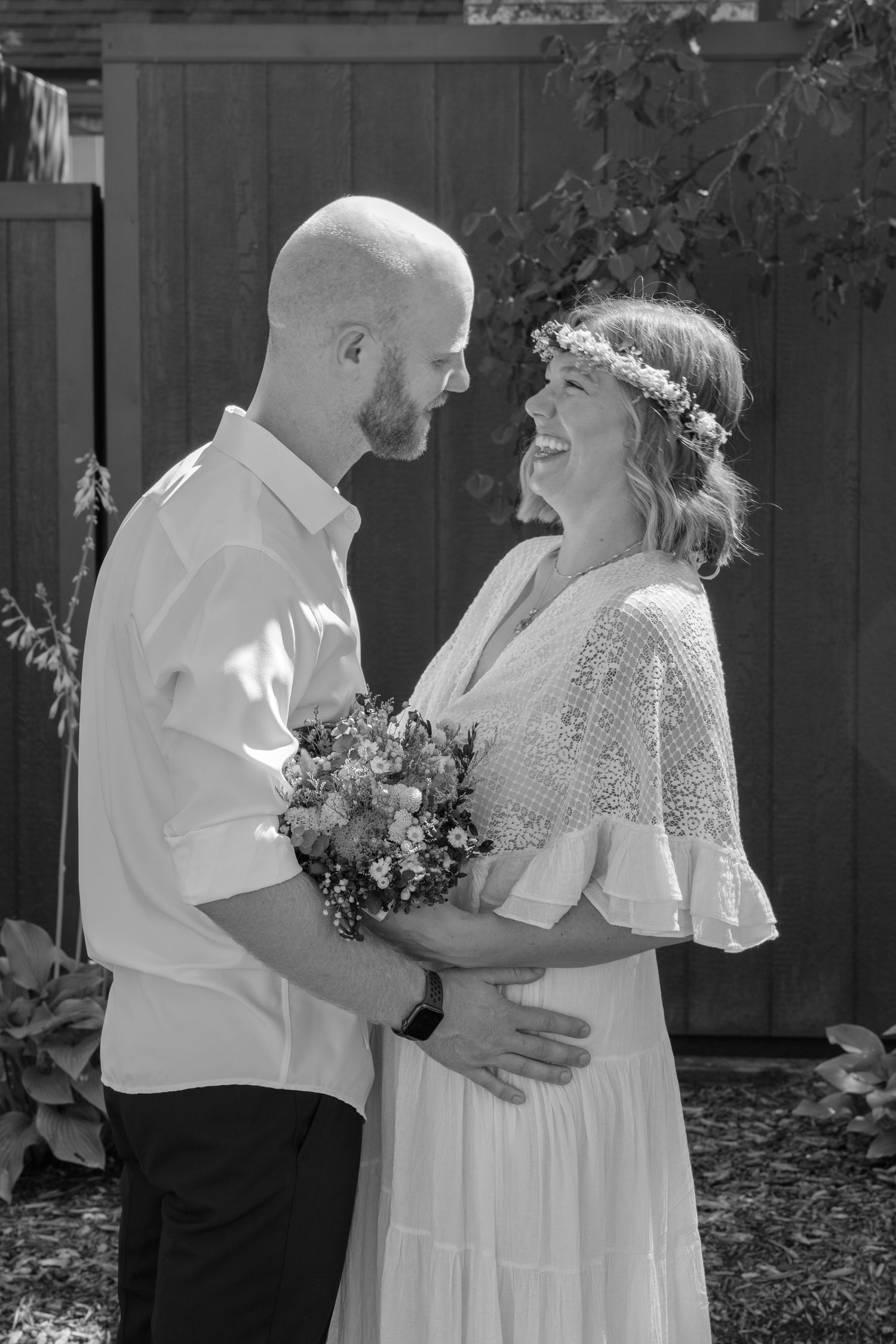 A romantic black and white wedding photo of a couple sharing a joyful moment while holding a floral bouquet.