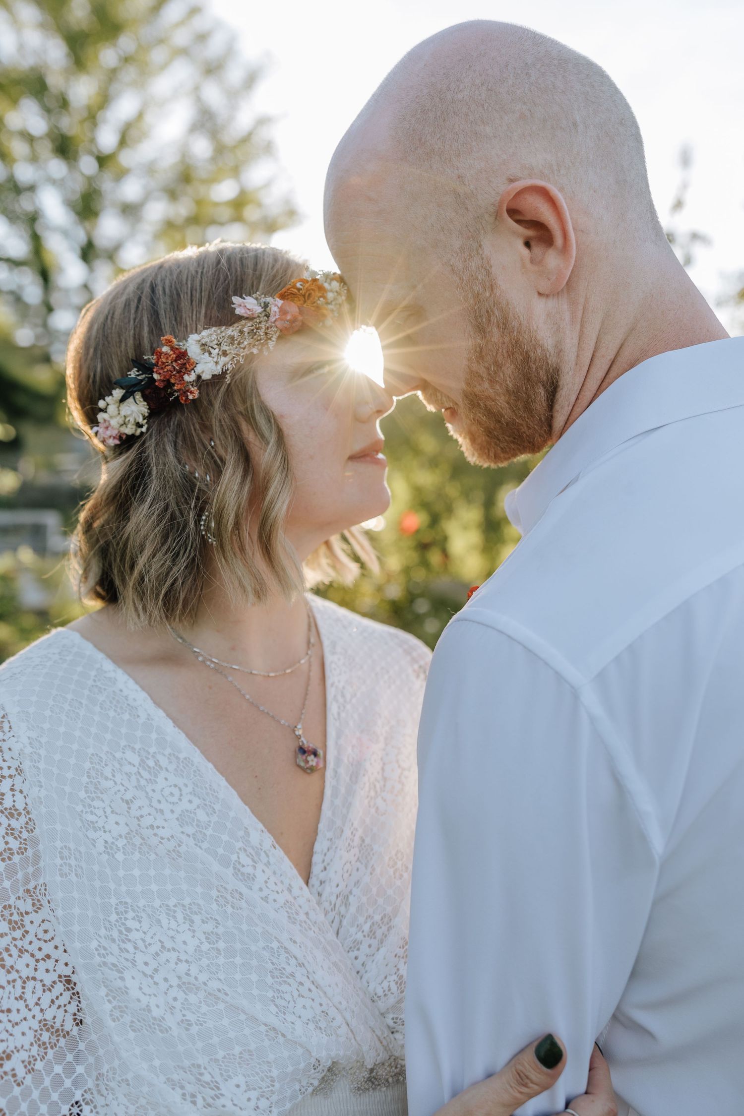Romantic sunset wedding portrait with sunlight streaming through trees in golden hour.