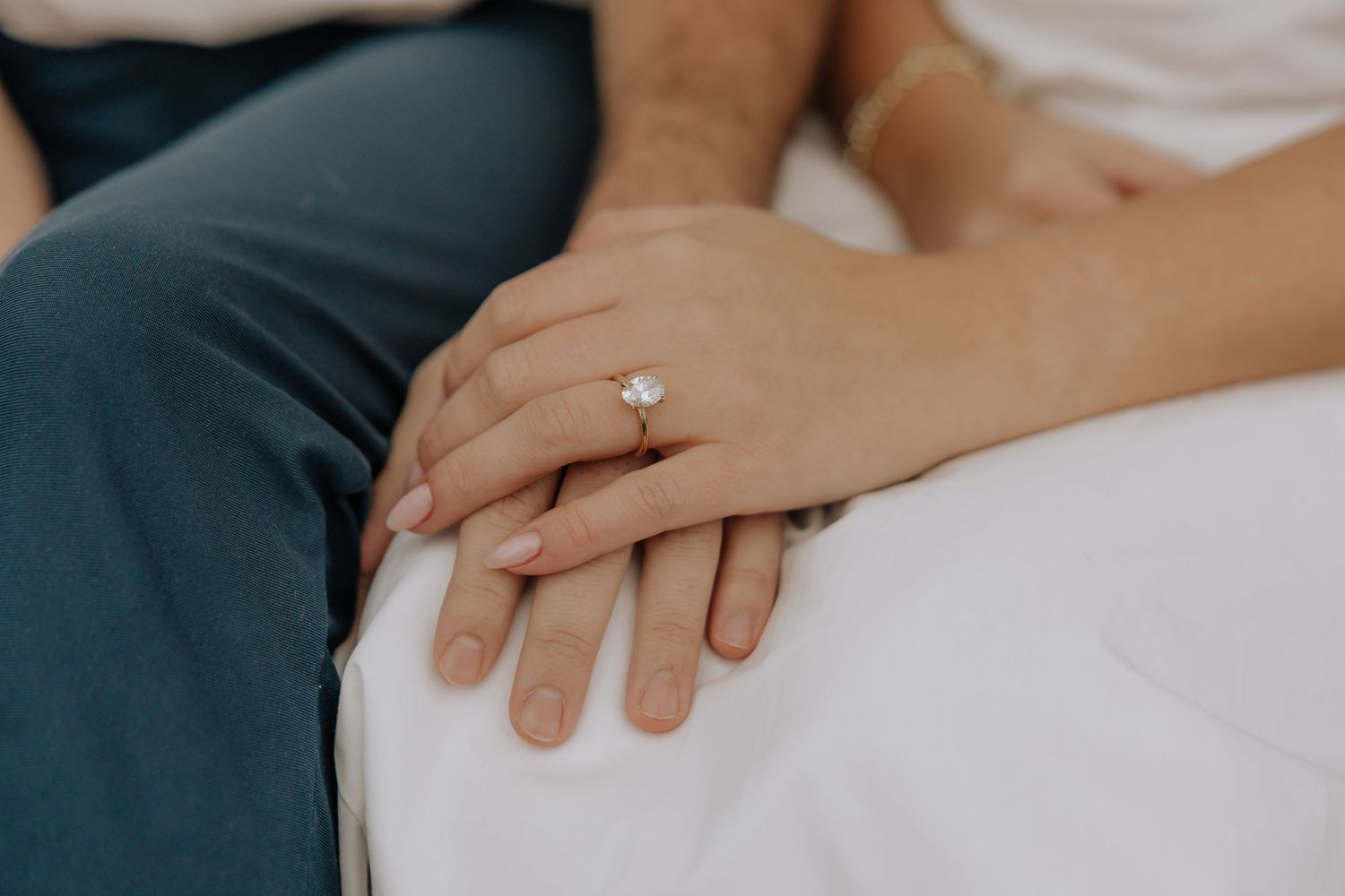 Close-up view of hands displaying engagement rings against a soft neutral background.