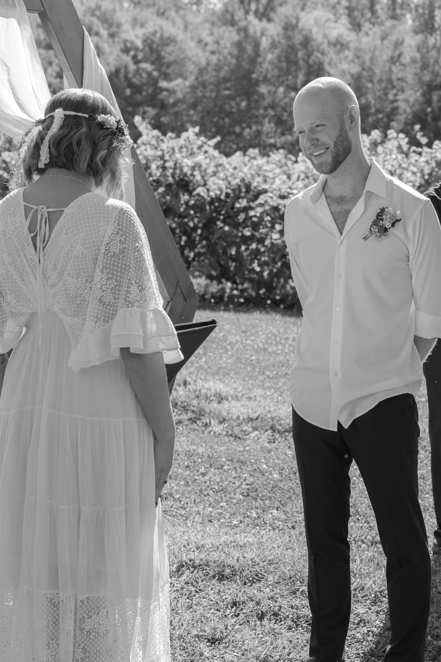 A group of people wearing white tops and black pants stand together in a sunny outdoor garden wedding setting.