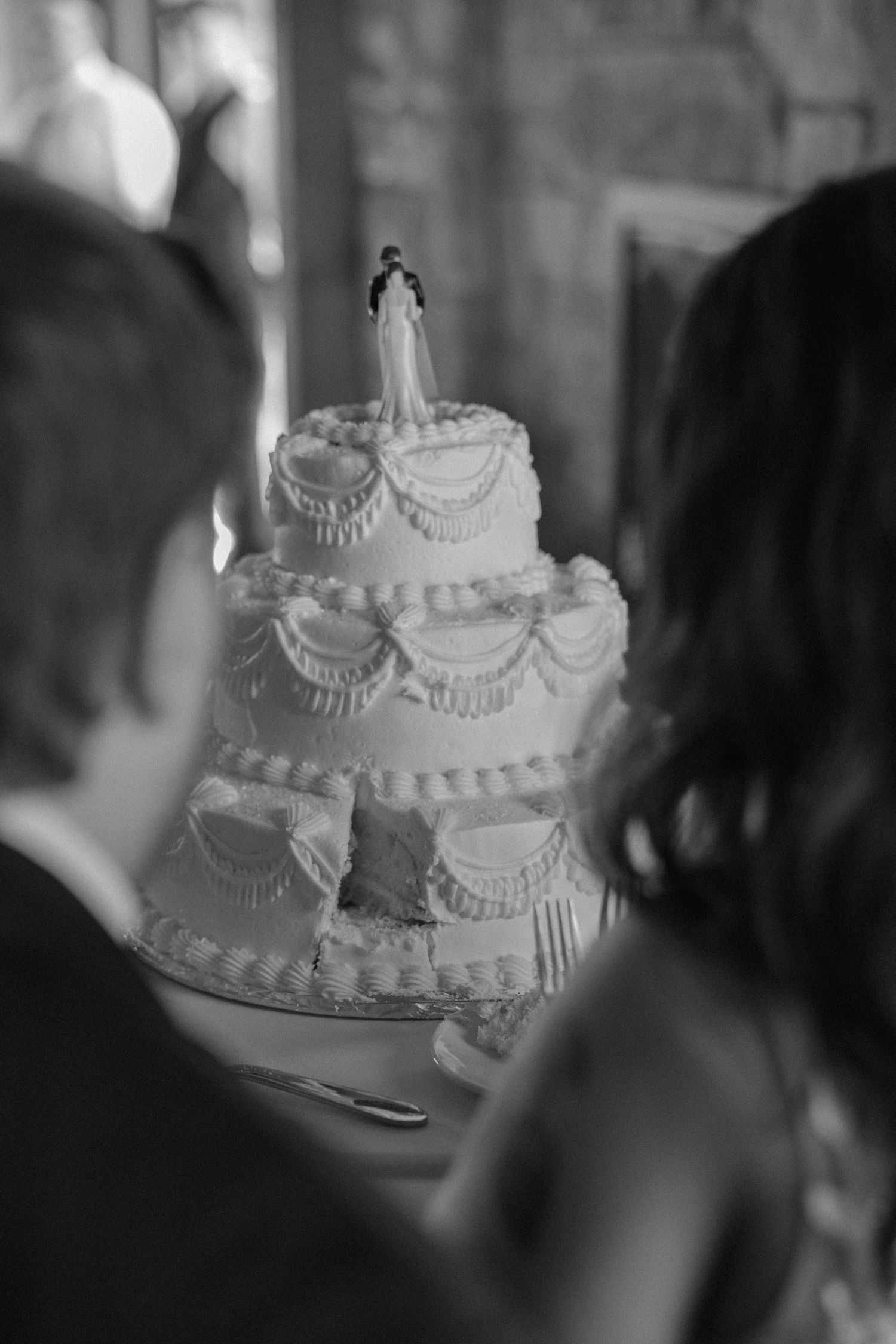 A traditional white wedding cake with ornate piping and multiple tiers is displayed in black and white photography.