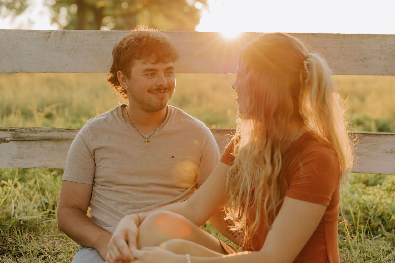 A couple sits together outdoors during golden hour, sharing intimate moments in a warm sunlit setting.