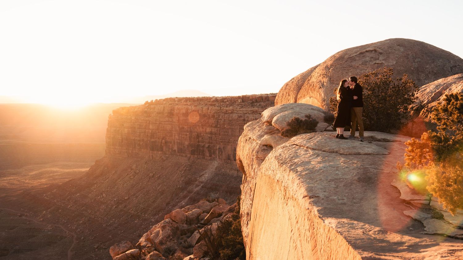 Couple stands on cliff edge during golden hour at a scenic overlook.