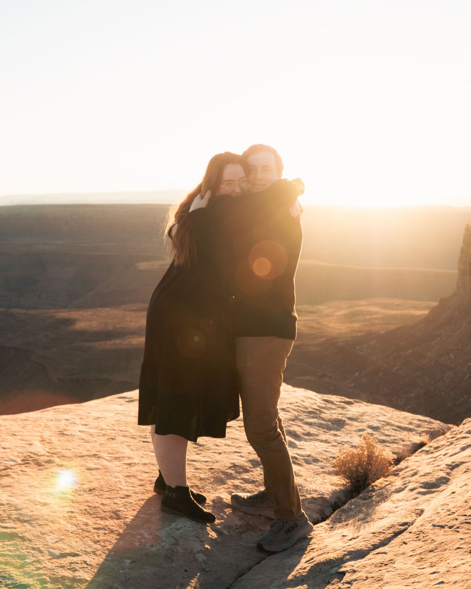 Two people embracing on desert cliff edge during sunset.