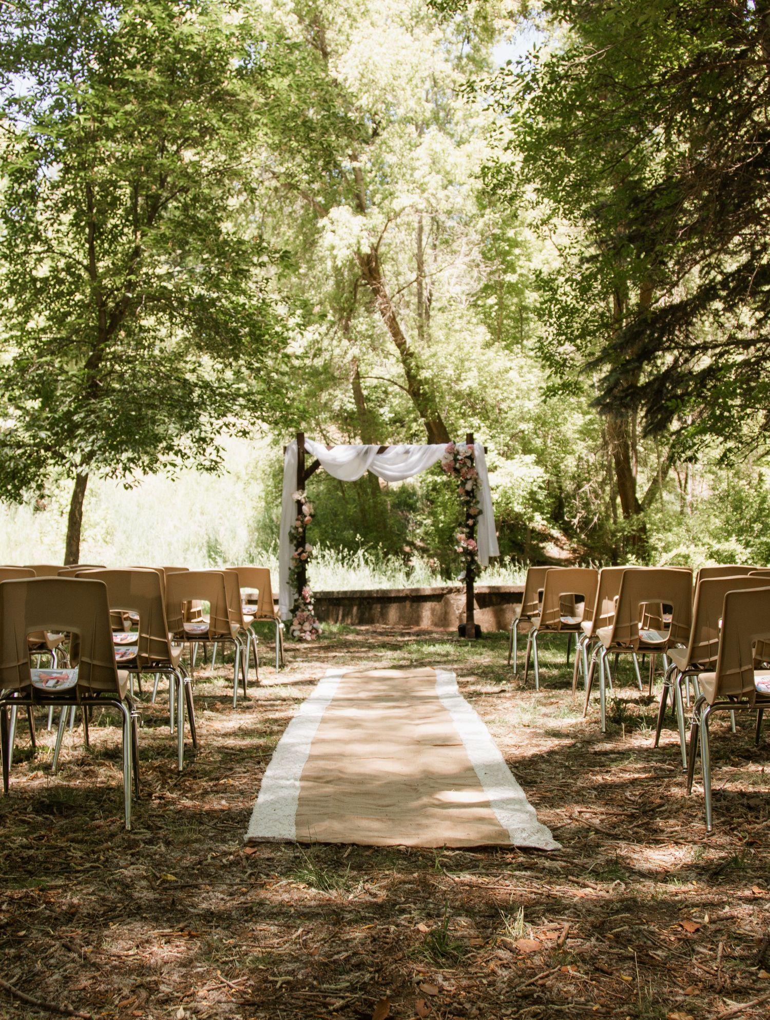 Outdoor wedding venue with rustic seating arranged among trees in natural setting.