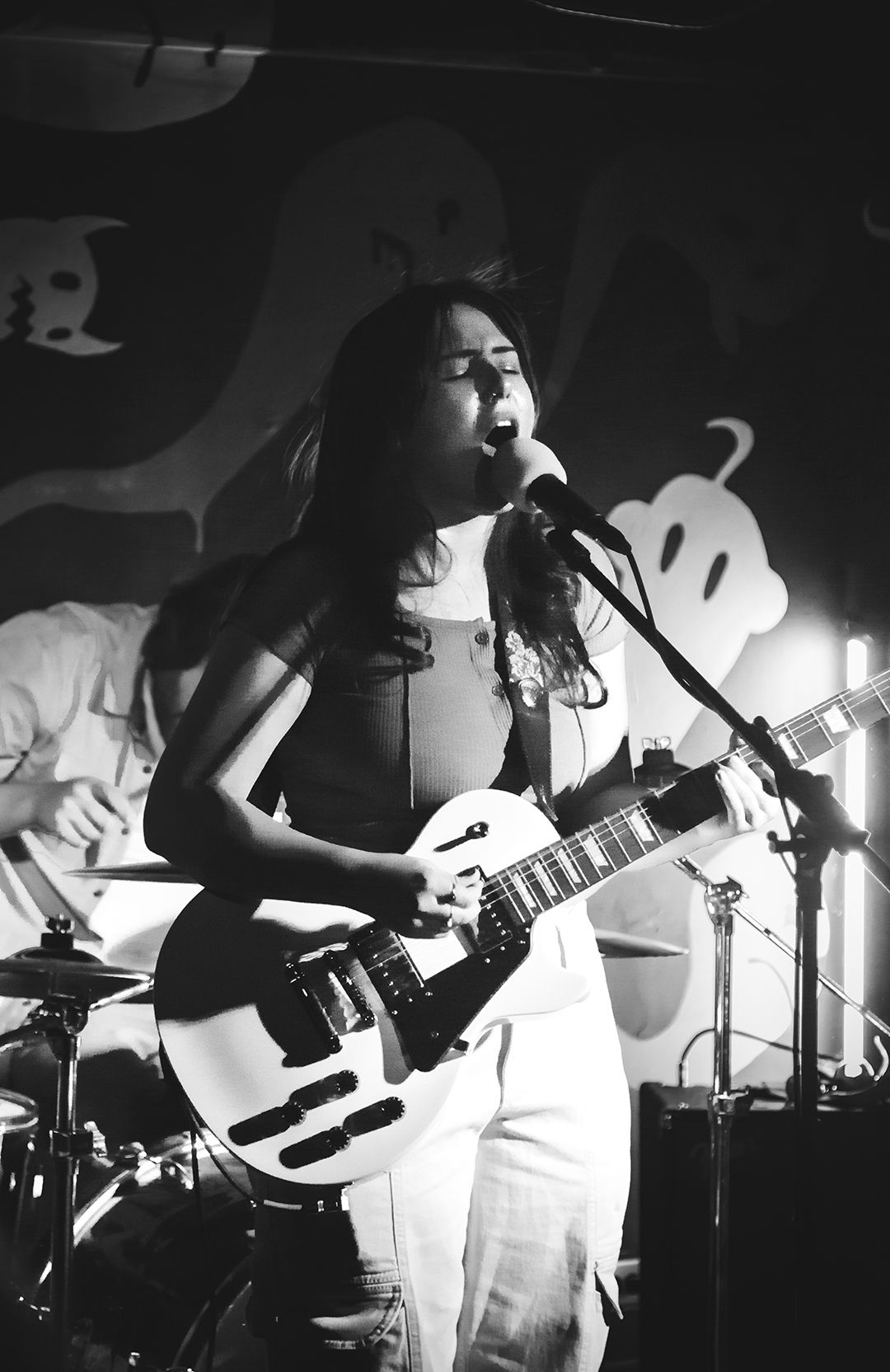 Concert performer plays electric guitar on stage with ghost decorations in background.