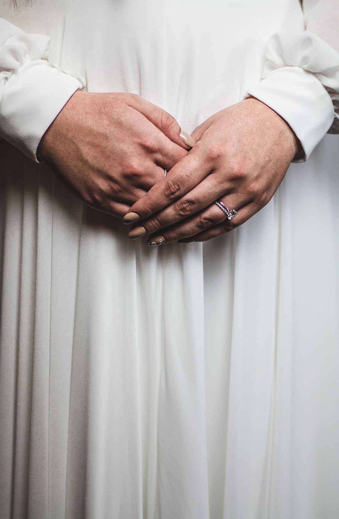 Close-up of hands wearing wedding rings against a white dress fabric background.
