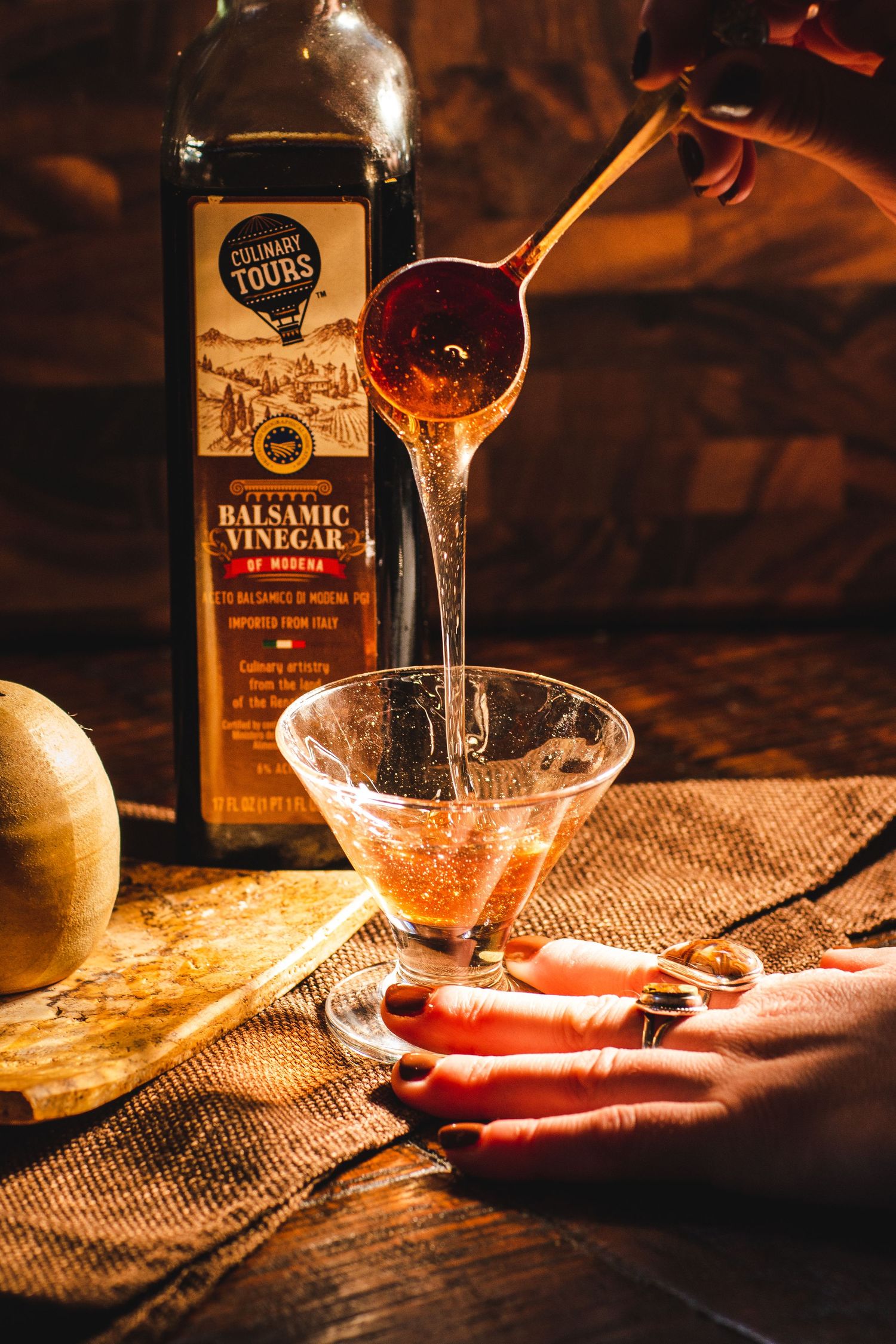Pouring balsamic vinegar into glass bowl in warm, moody lighting.