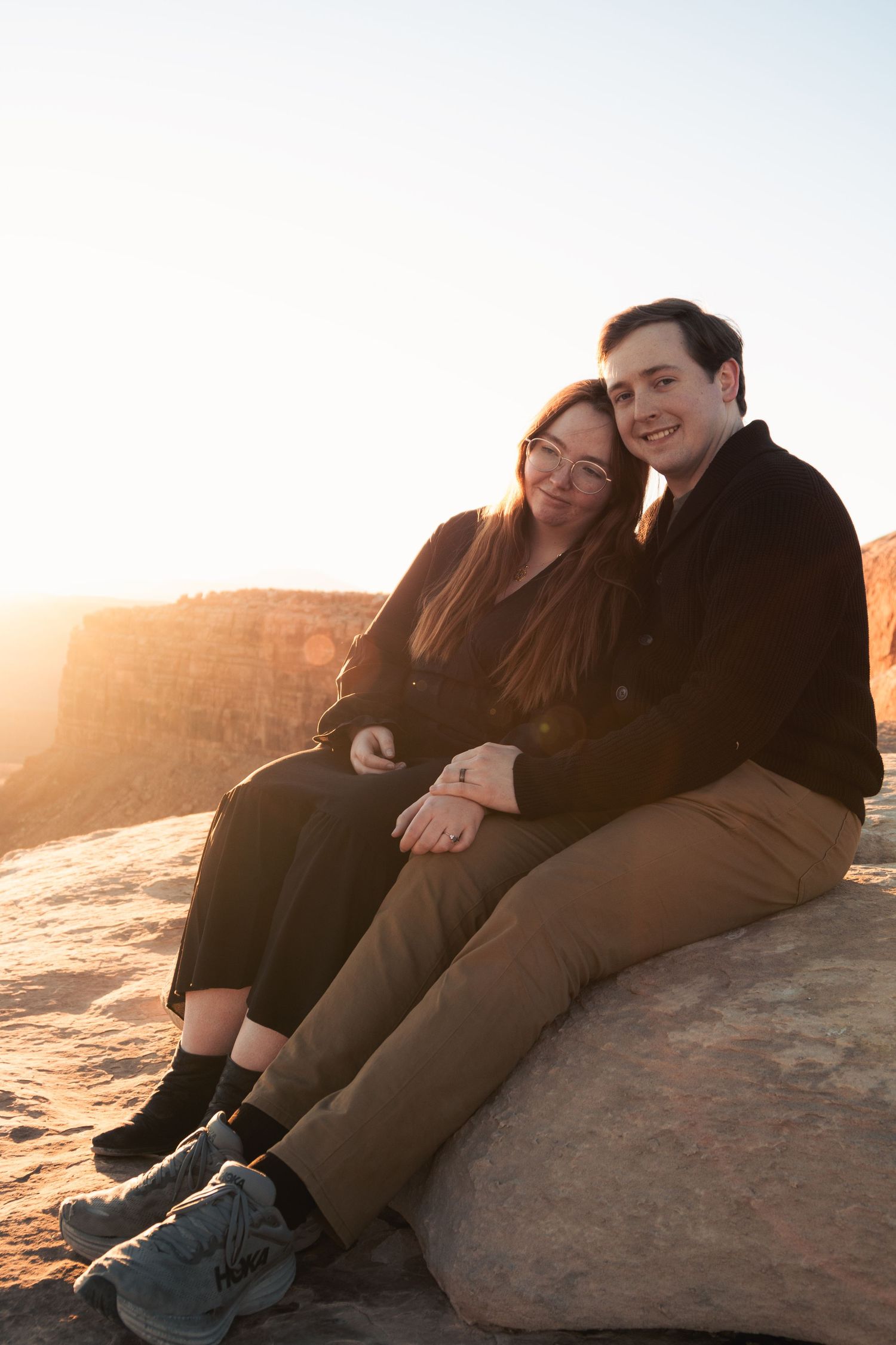 Couple relaxes together on rocky ledge during golden hour in the desert.
