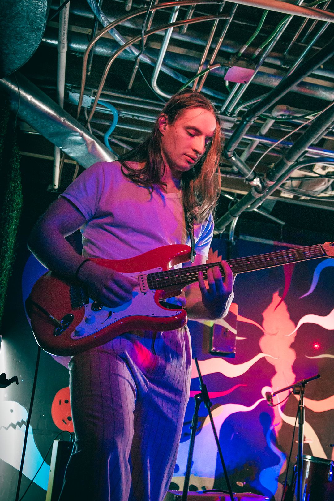 Musician performing on stage with electric guitar under blue and red stage lights.