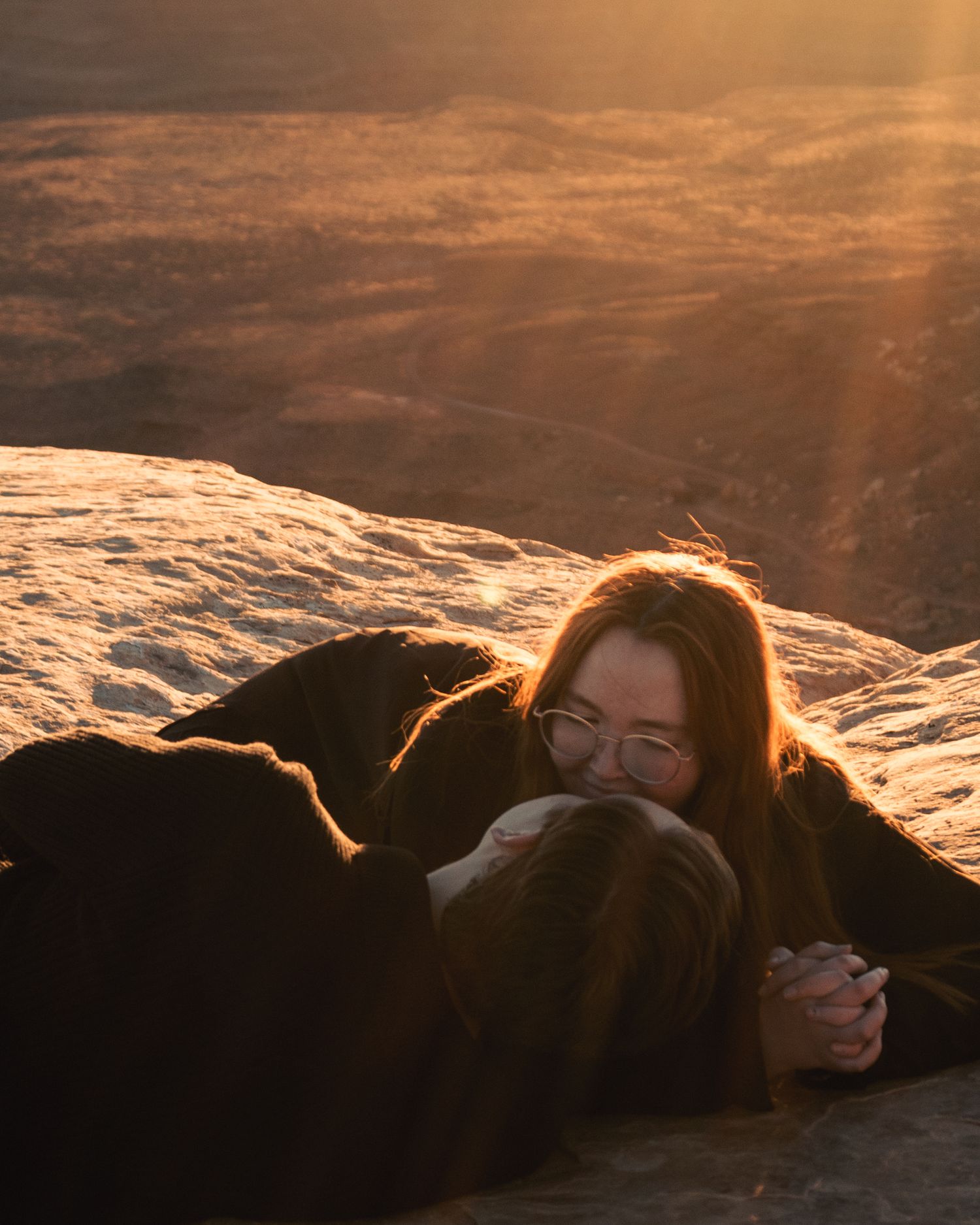 Couple lying together on rocky cliff during golden sunset.