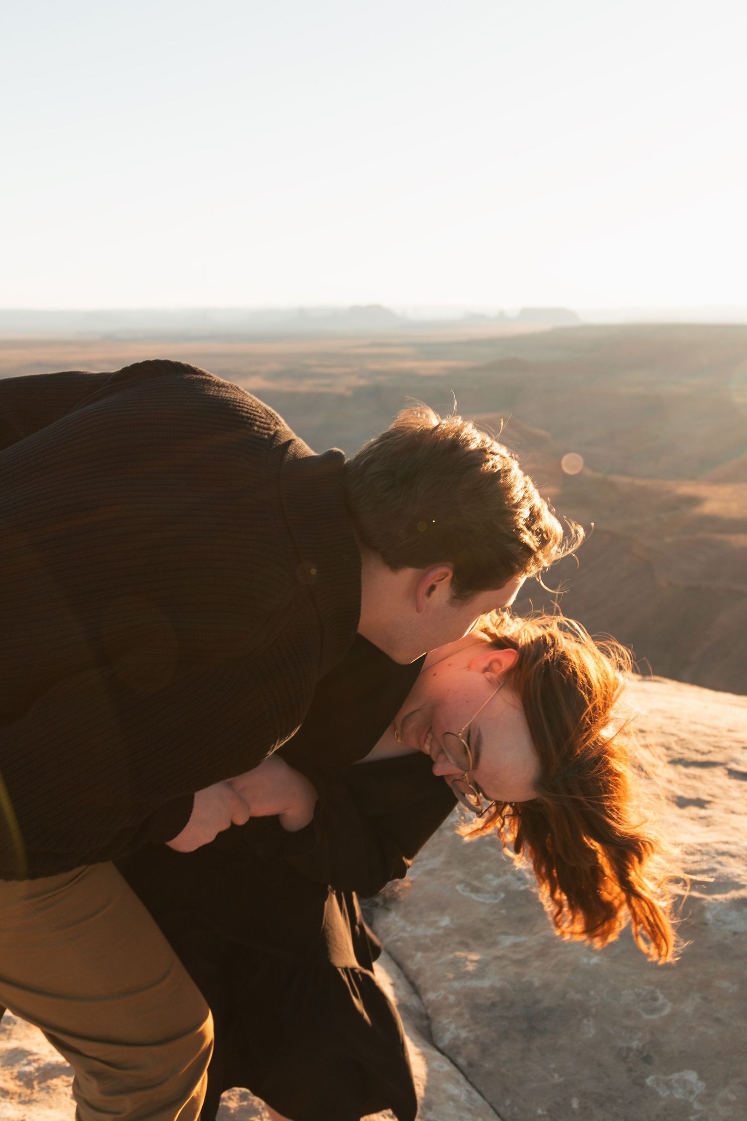 Couple shares intimate moment on cliff edge during golden hour in desert landscape.