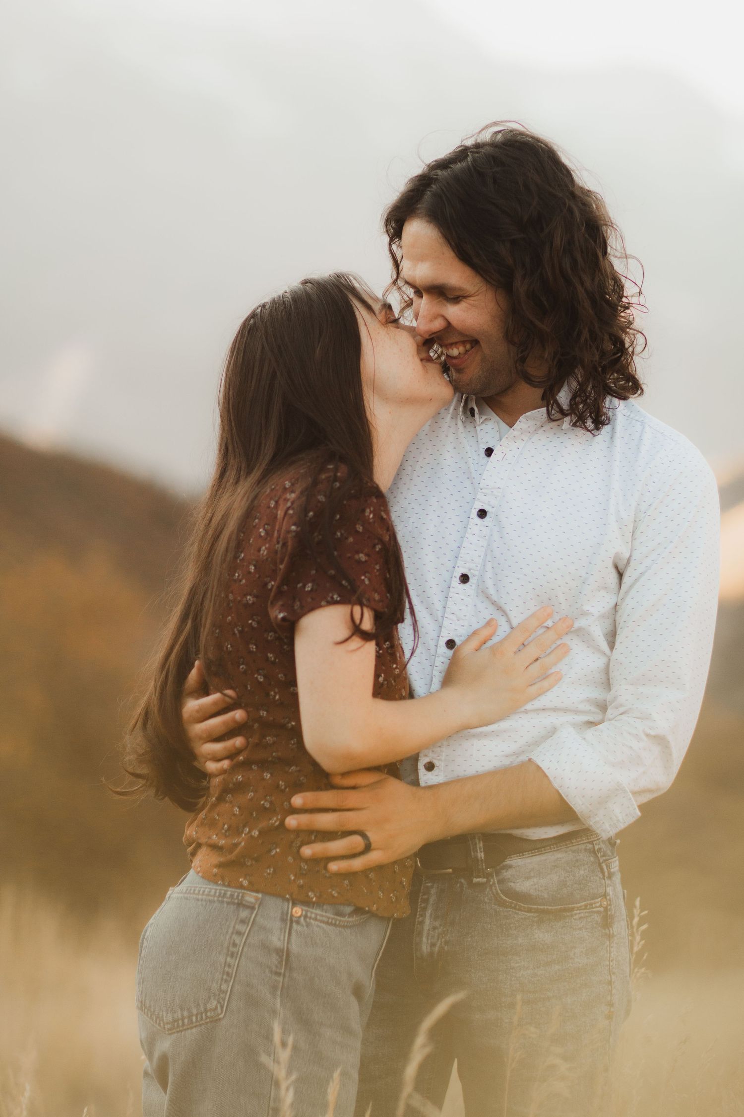 A romantic couple embraces in a golden field during sunset, creating an intimate and dreamy outdoor portrait.