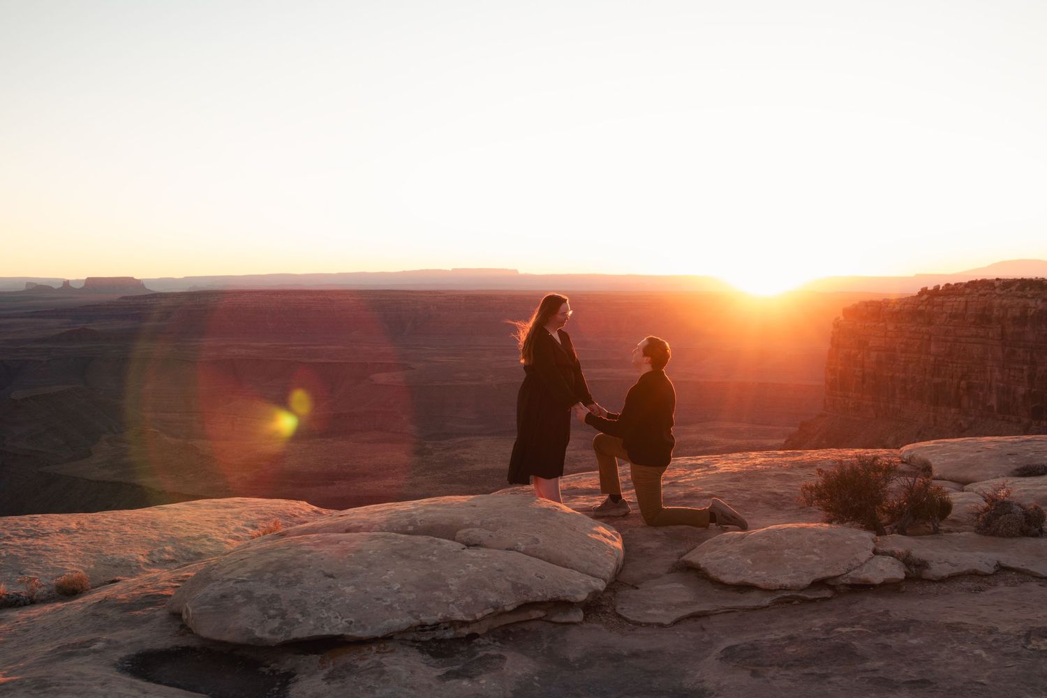 A couple sits on rocky terrain during a colorful mountain sunset.