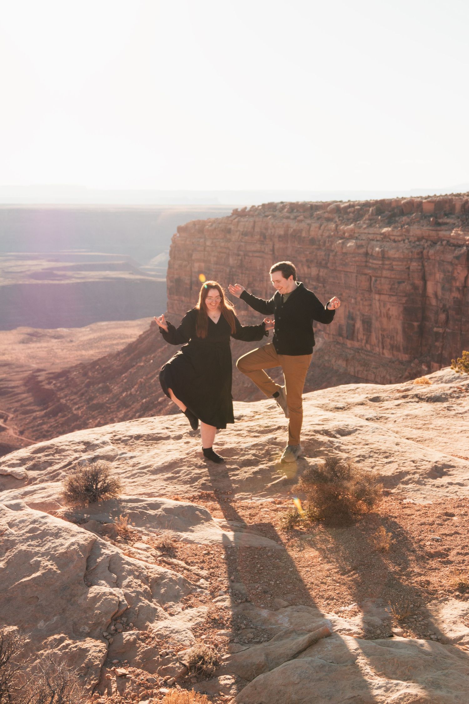 Couple dancing joyfully on edge of scenic desert canyon overlook.