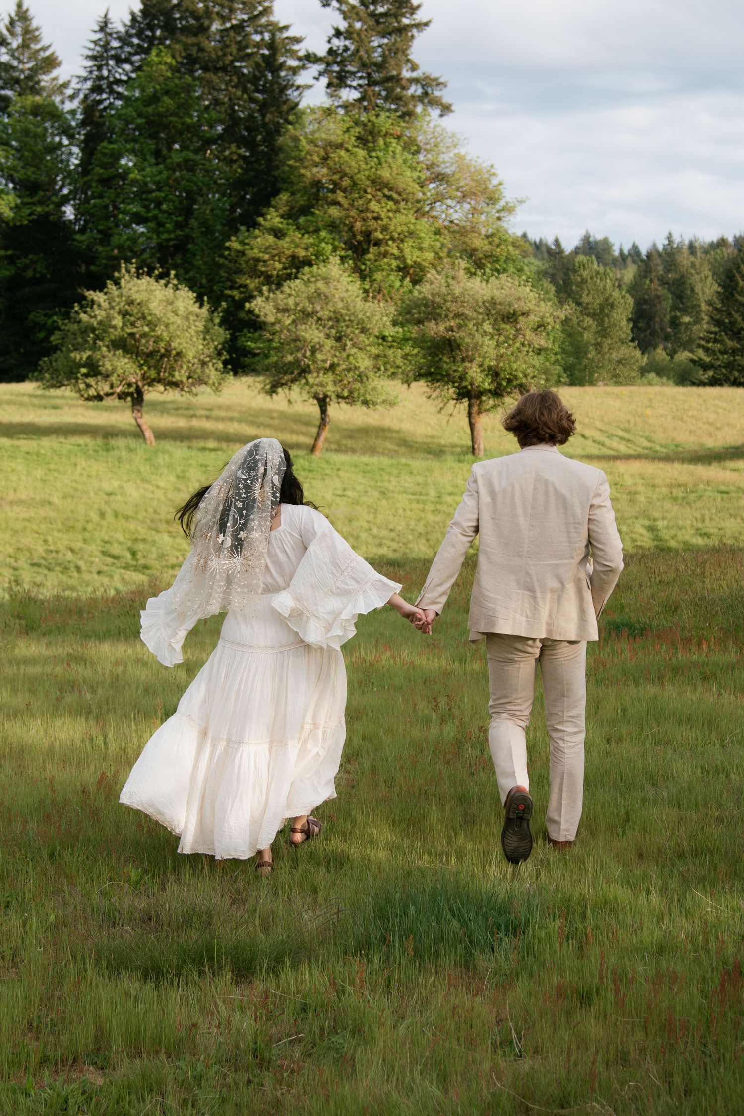 Two figures in white and beige walk through a lush green meadow.
