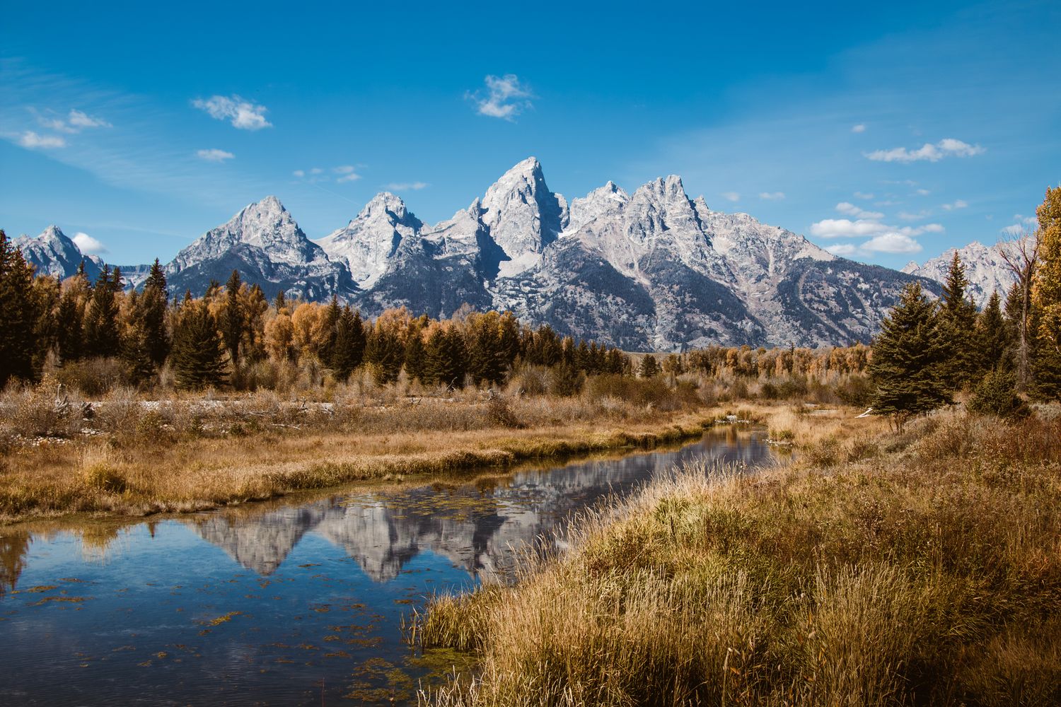 Panoramic mountain landscape with snow-capped peaks reflected in calm water.
