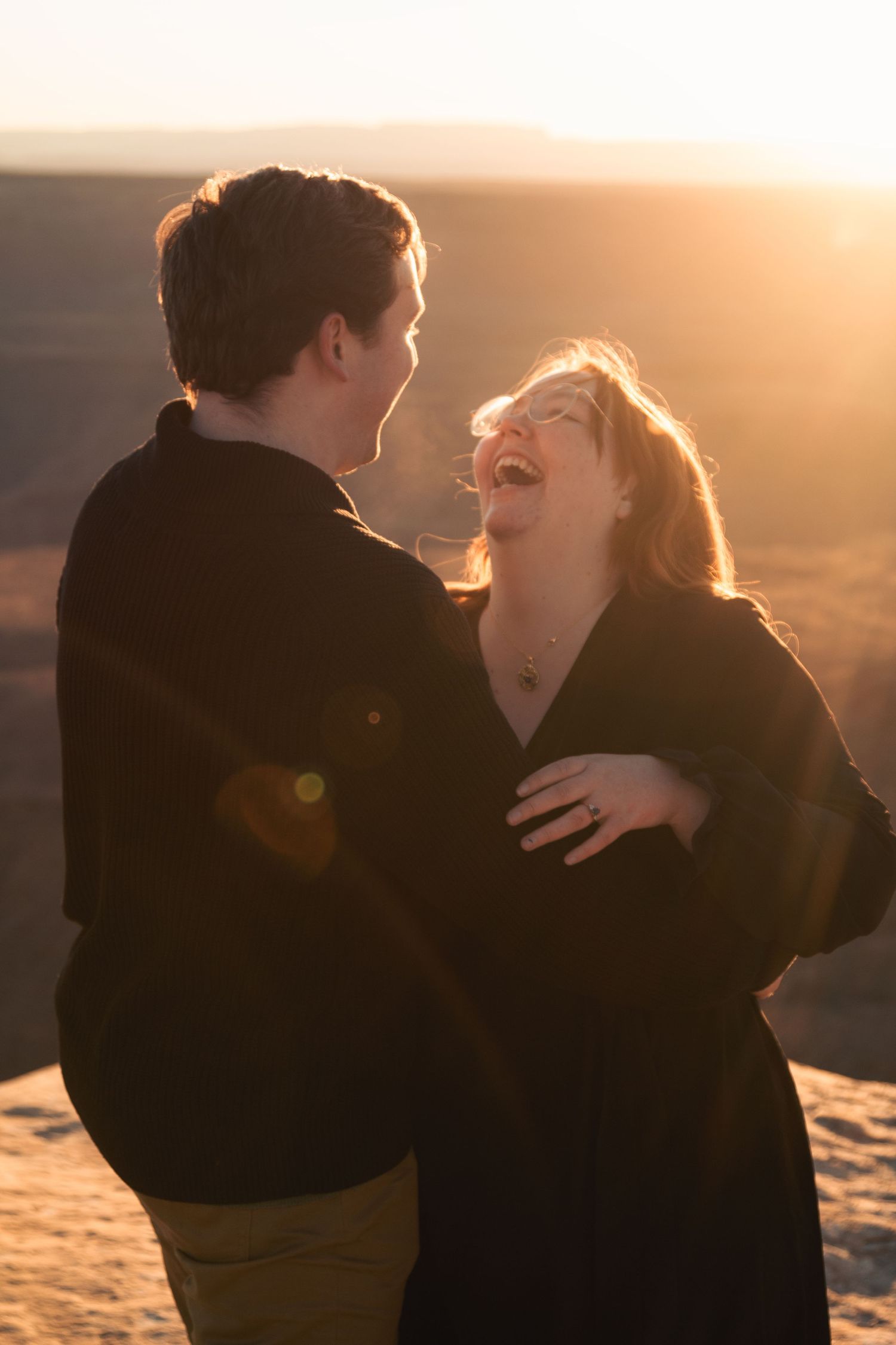 Couple laughs together during golden hour desert photoshoot with sun flare.