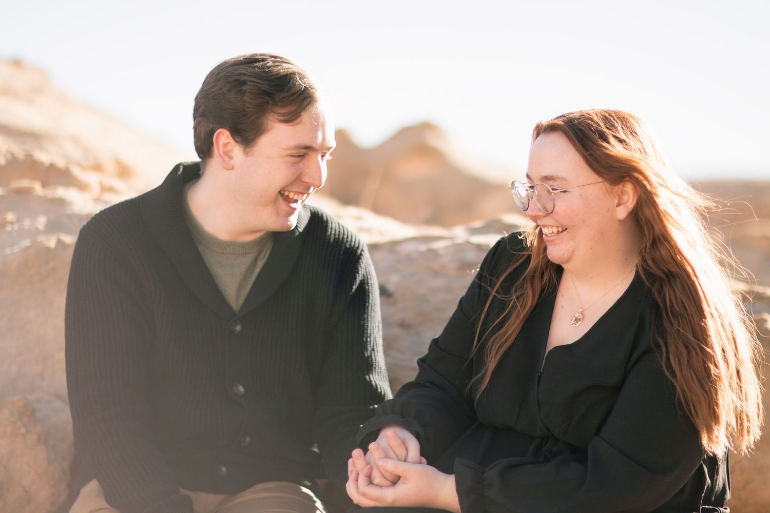 Couple embraces and laughs together during sunrise photoshoot with warm backlighting.