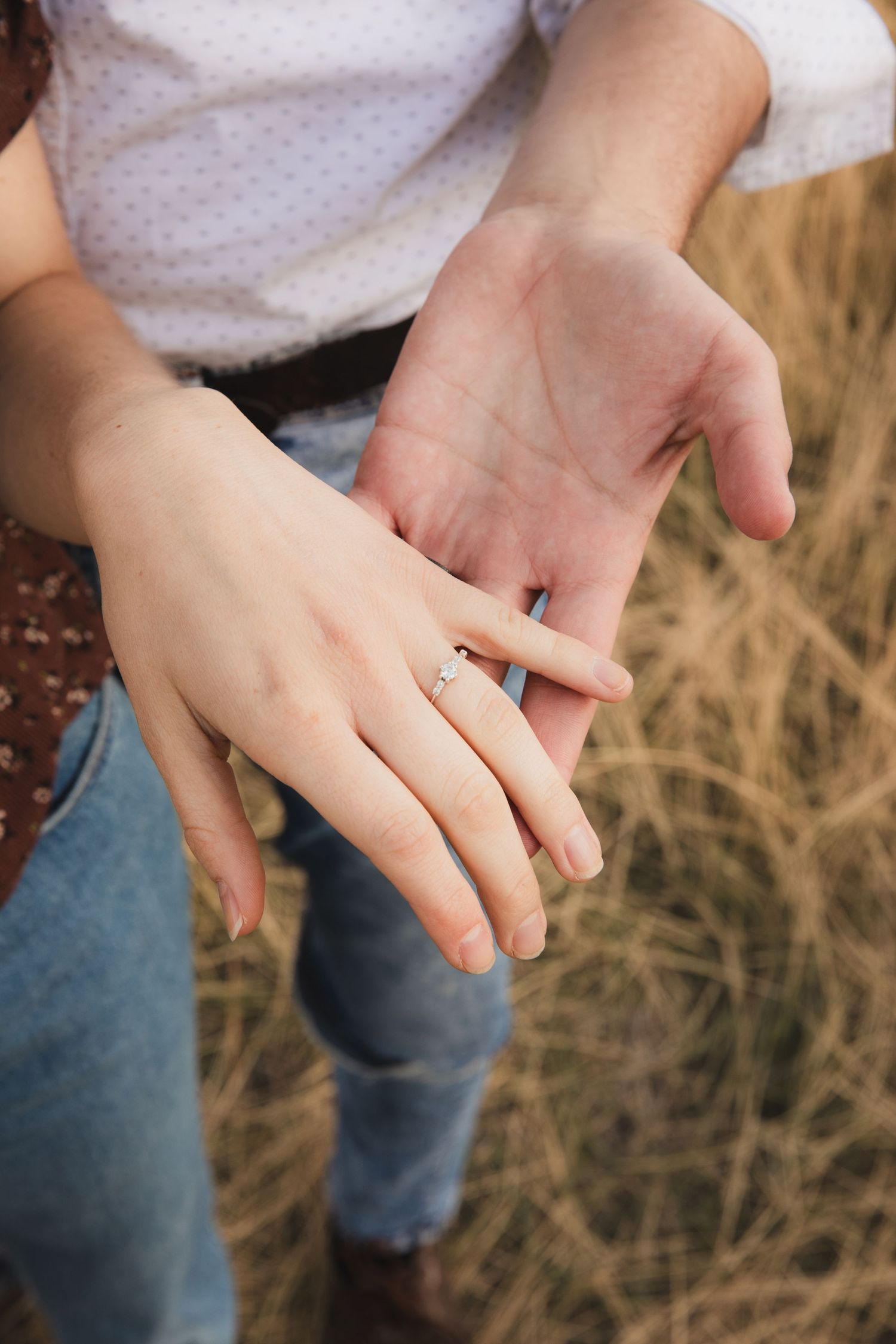 Close-up view of hands exchanging rings during an outdoor wedding ceremony in a rustic field setting.