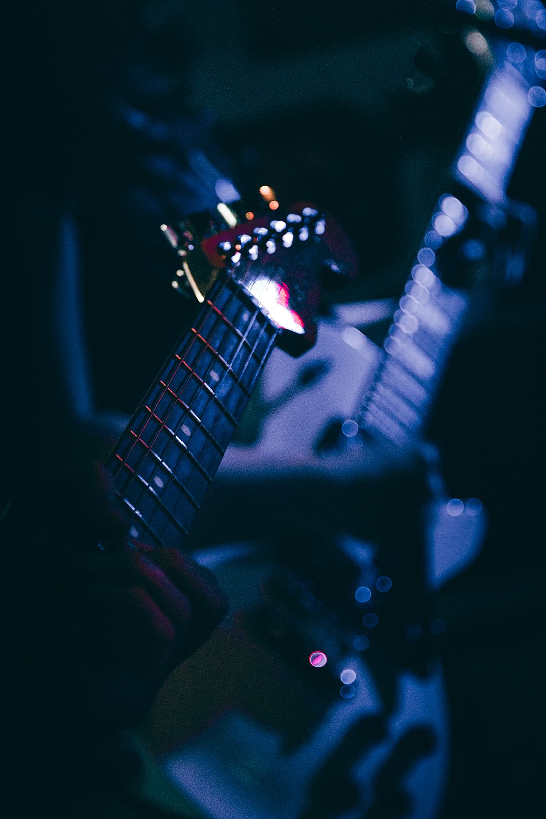Close-up of guitar fretboard and strings in dramatic blue lighting.
