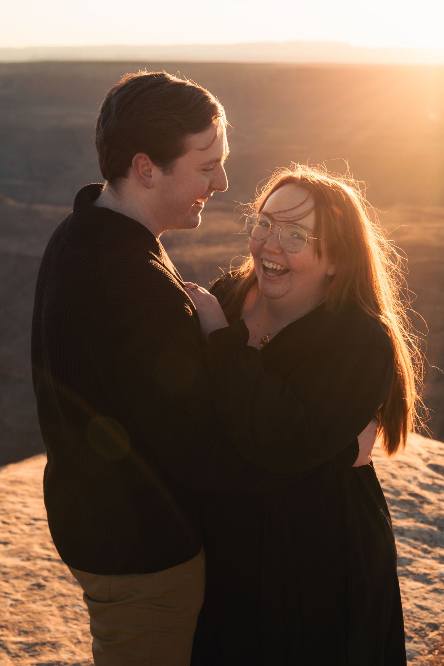 Golden sunlight illuminates a couple sharing tender moments on a desert cliff.