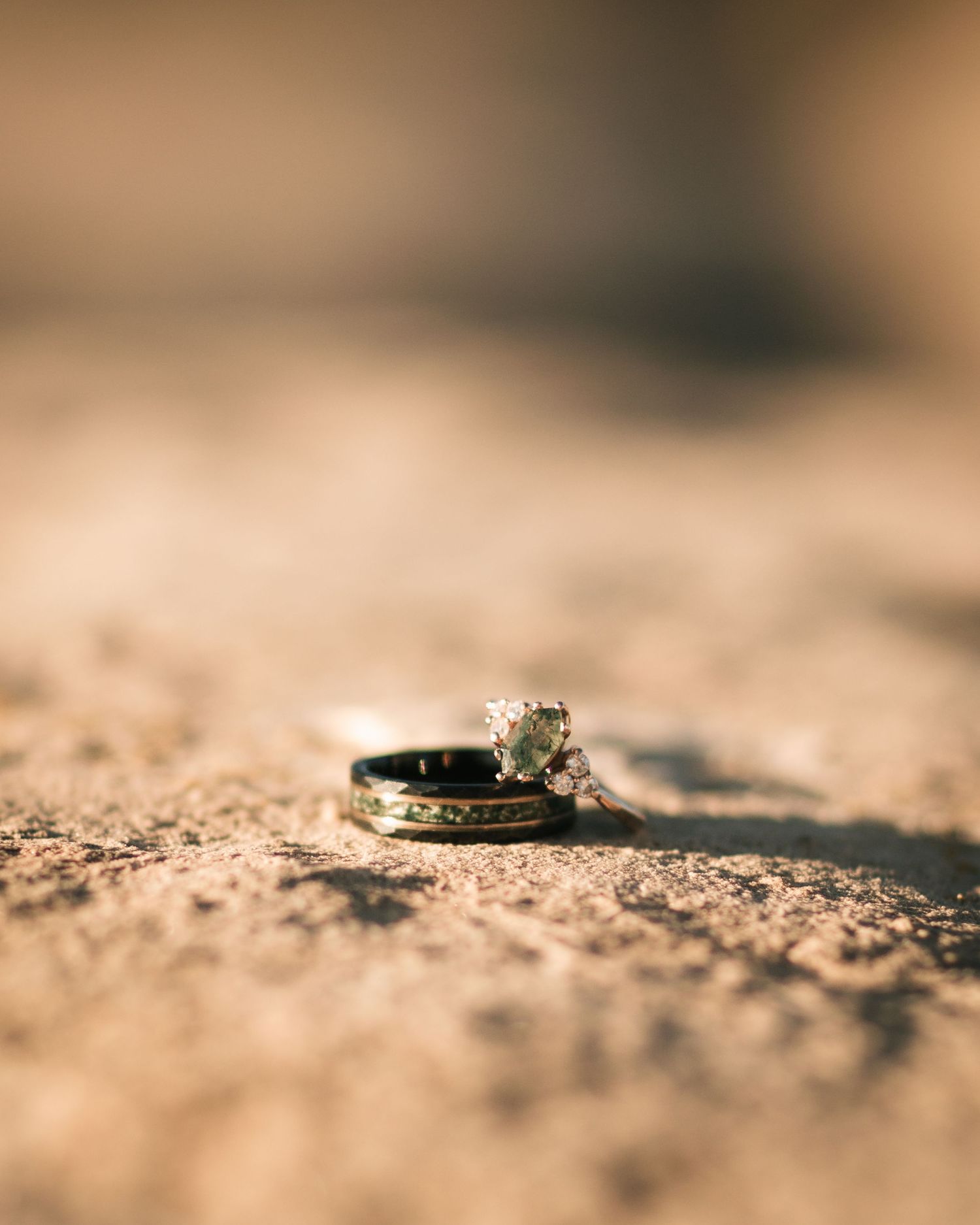 Diamond engagement ring photographed with shallow depth of field on a textured beige surface.