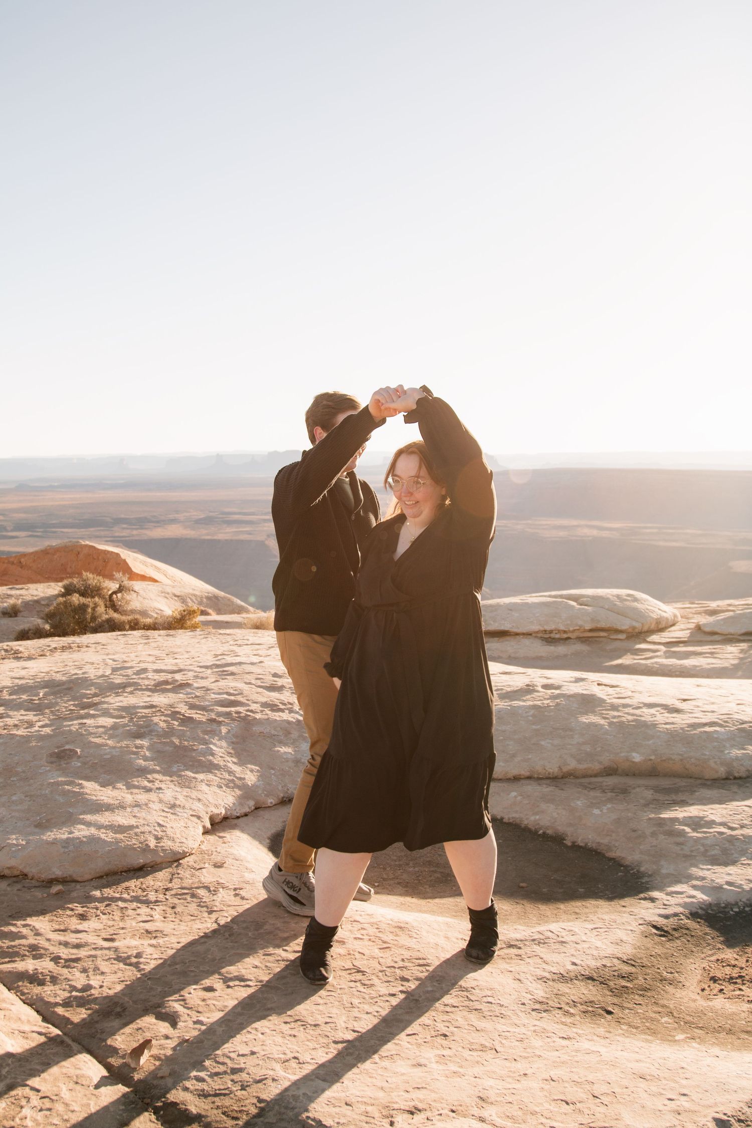 Two people dancing together on red rock cliff with desert vista behind them.