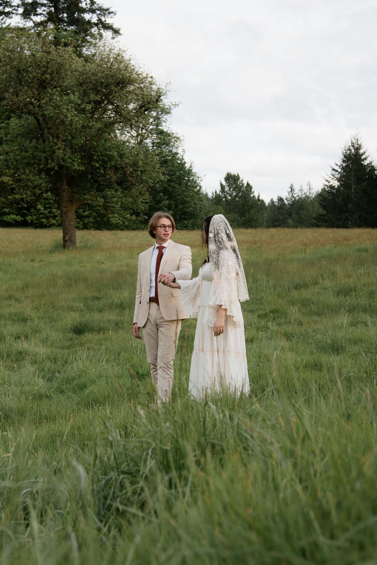 Two people in vintage-style clothing walk through a grassy field.