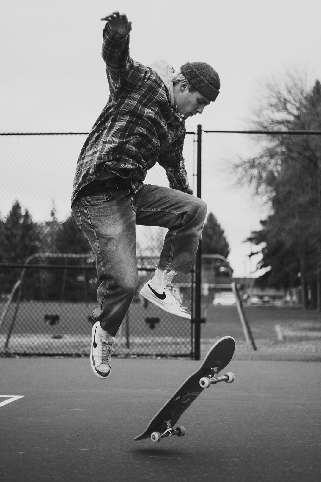 Skateboarder performing a trick jump in black and white at a basketball court.
