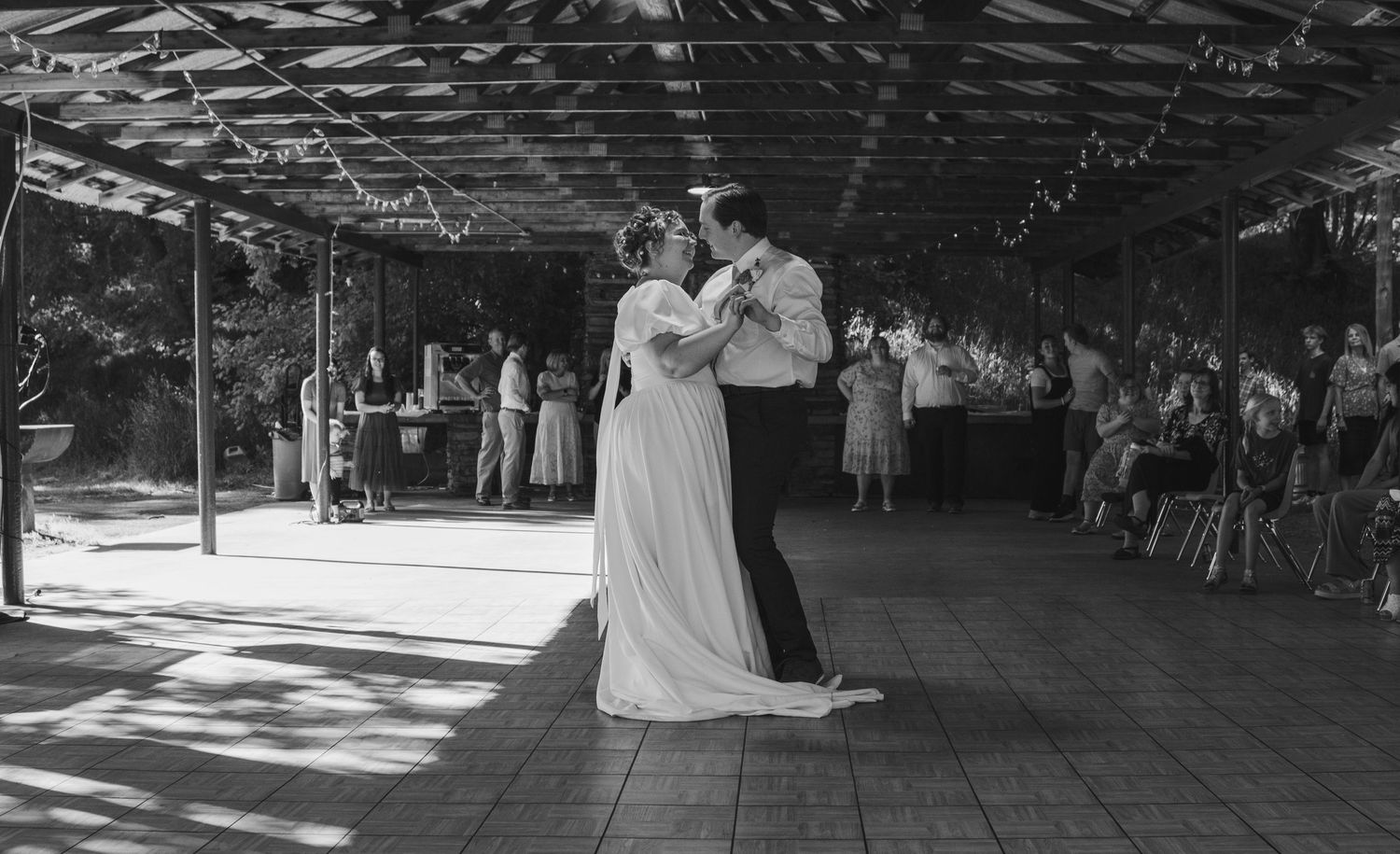 Black and white photo of wedding guests dancing in a covered outdoor venue.