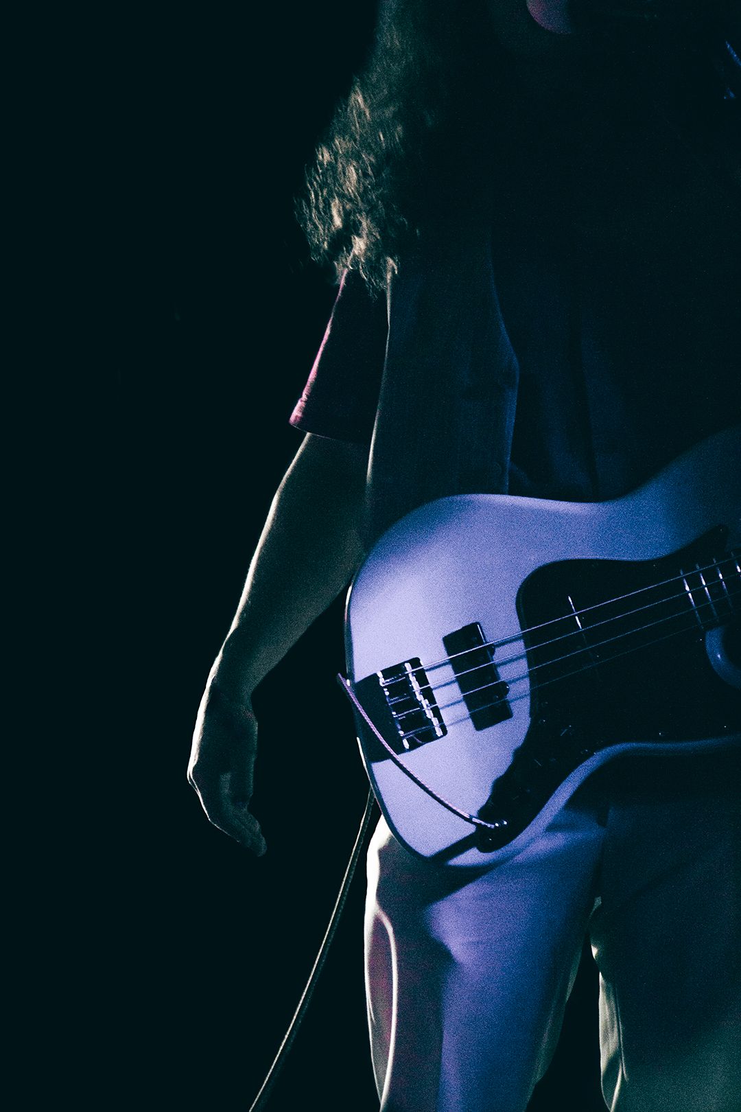 Silhouetted bass guitar against dark background with purple lighting.
