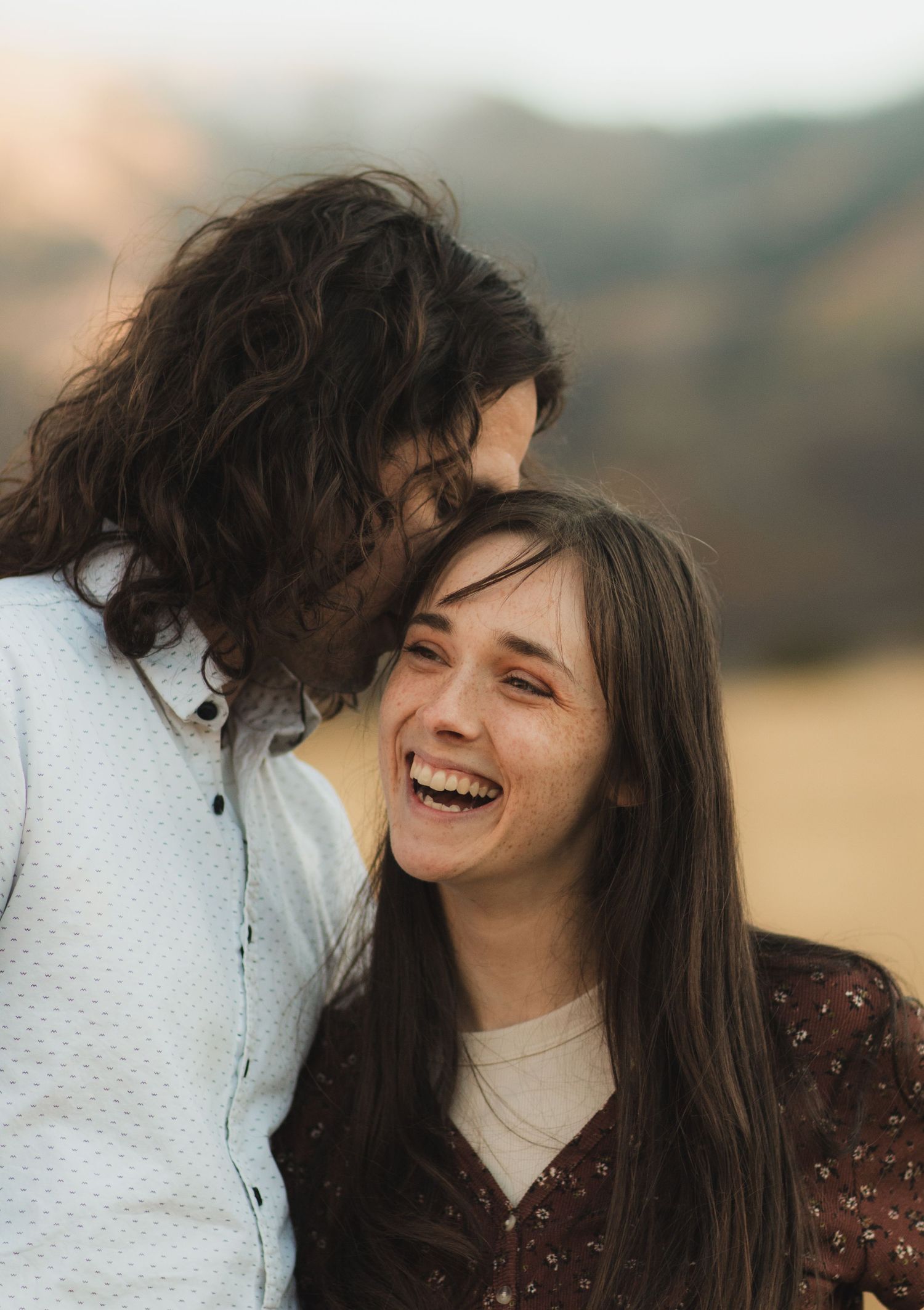 A couple shares joyful laughter together in a series of candid outdoor photos with a blurred natural background.
