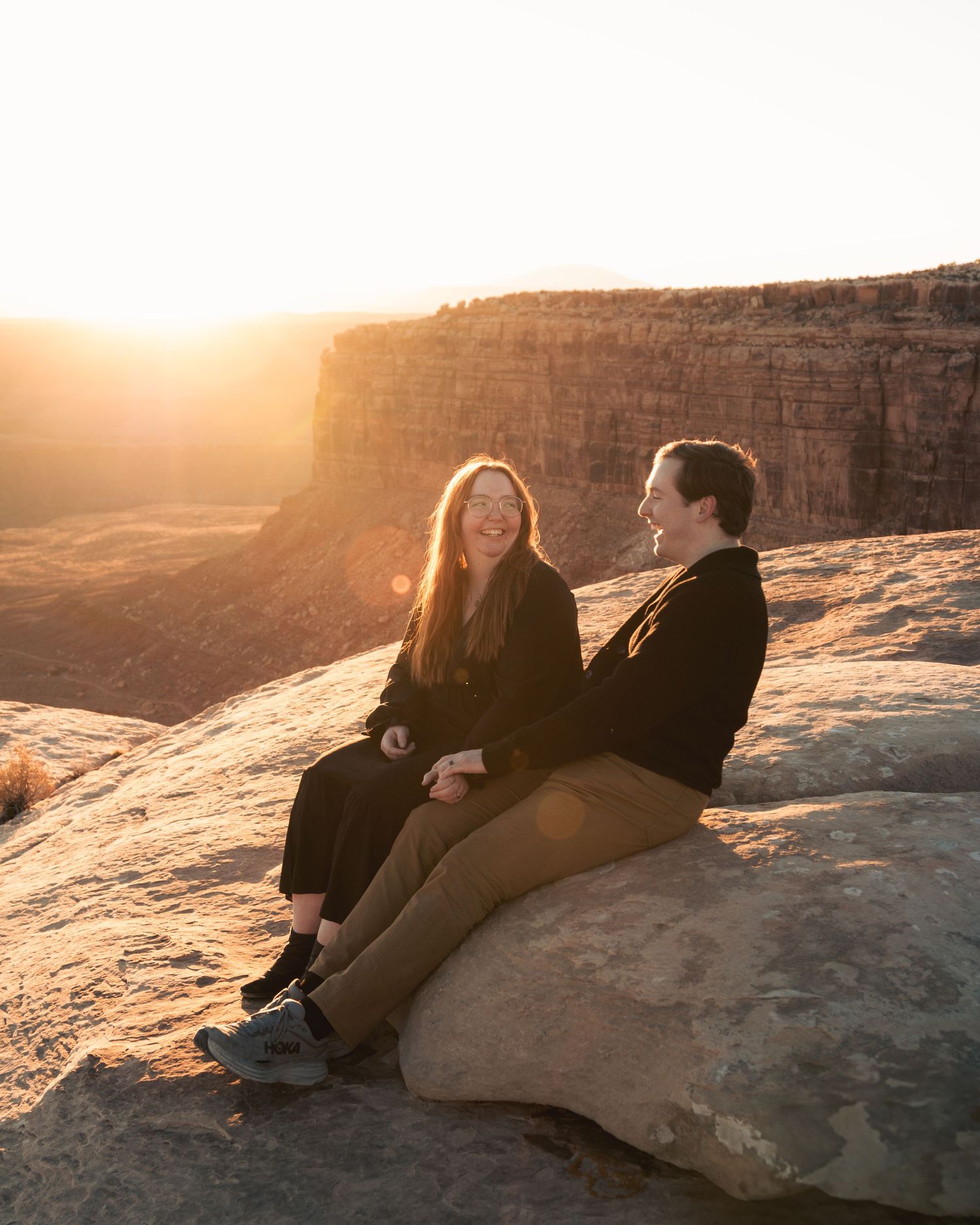 Two people sitting together on canyon edge during golden sunset.