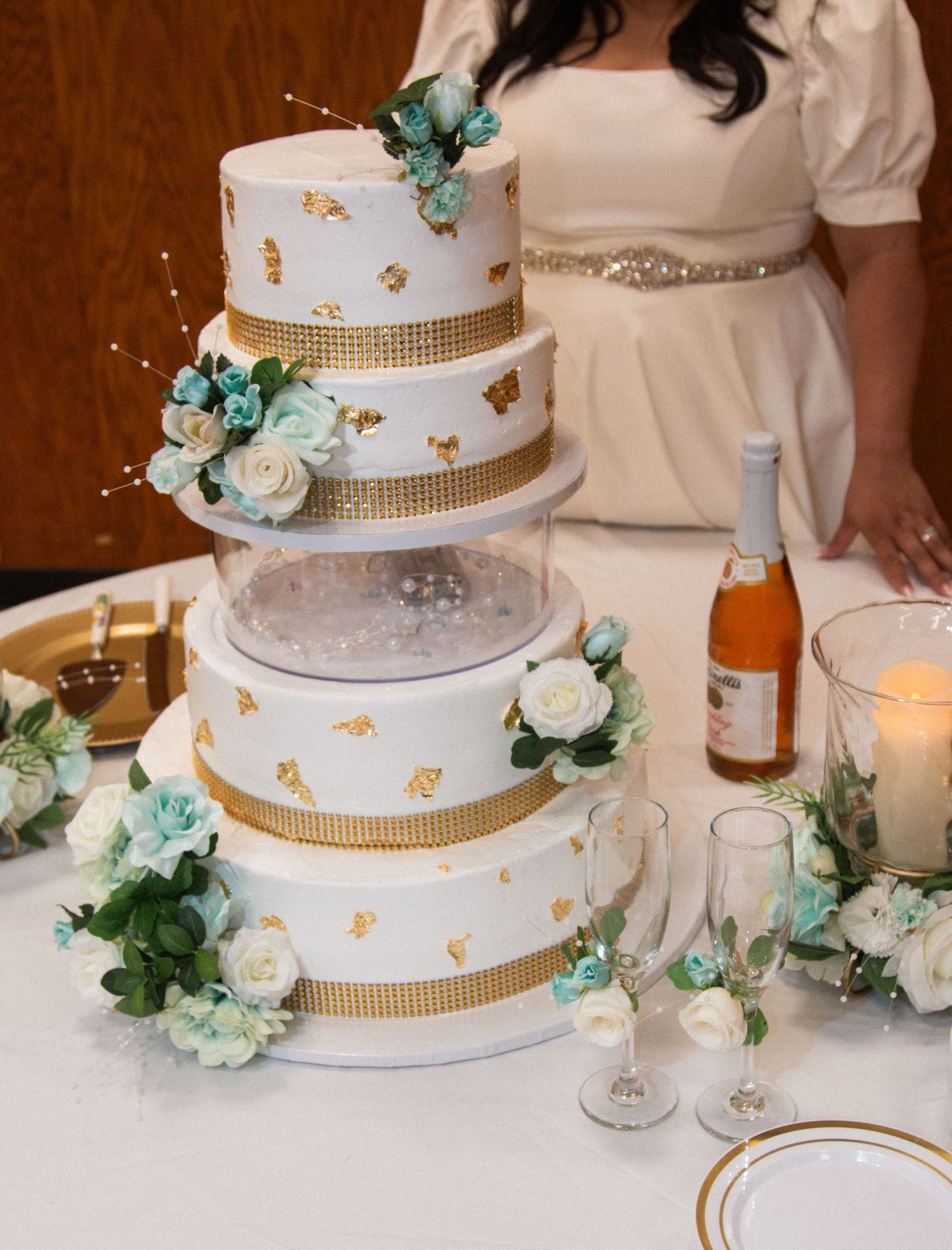 Elegant white and turquoise wedding cake decorated with gold accents and floral details.