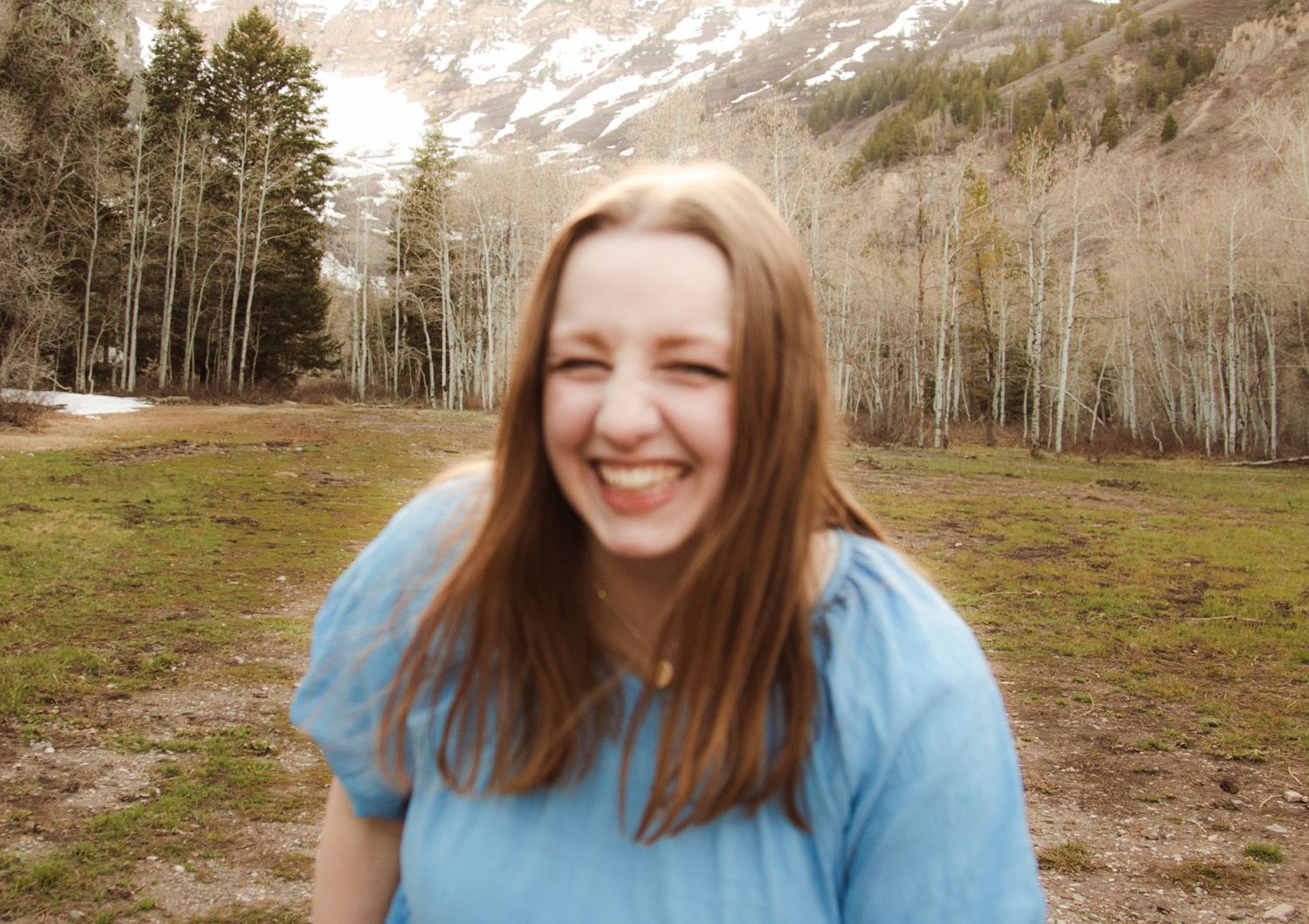 Person in light blue shirt smiling outdoors with scenic mountain background.