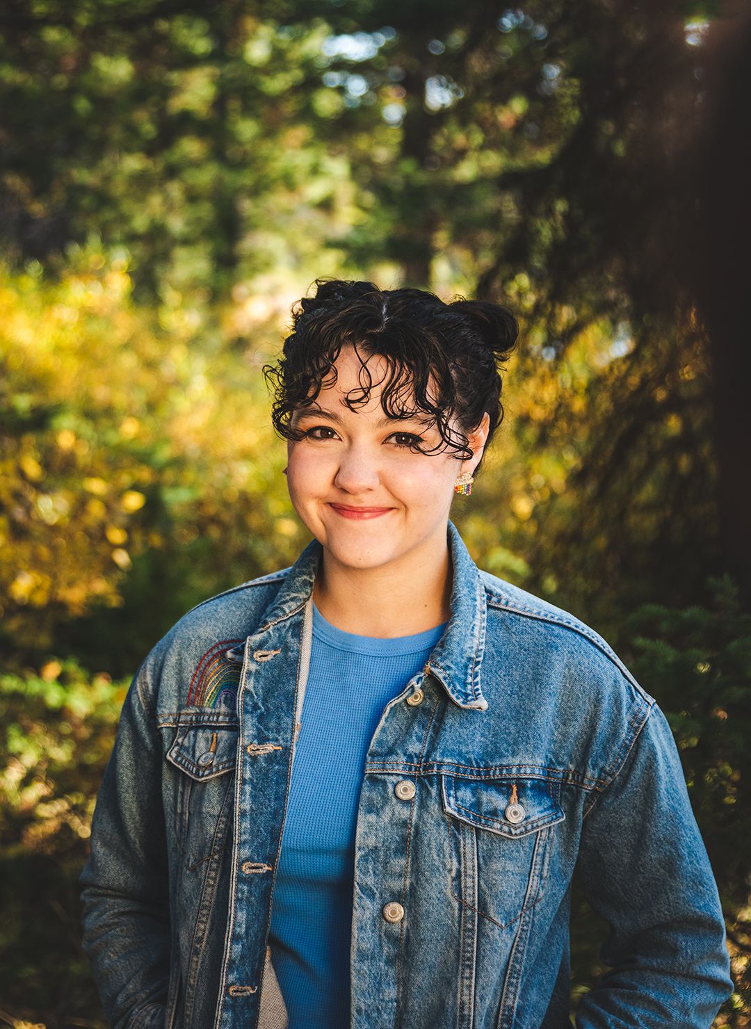 Casual portrait in denim jacket and blue shirt with natural sunlit background.
