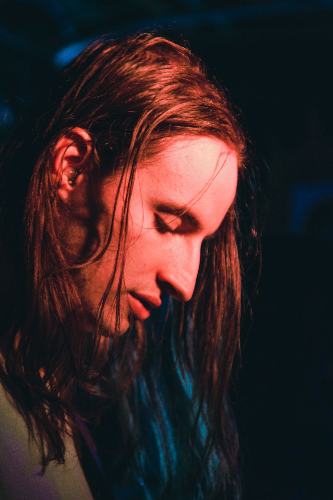 Profile view of performer with long hair illuminated by dramatic stage lighting.