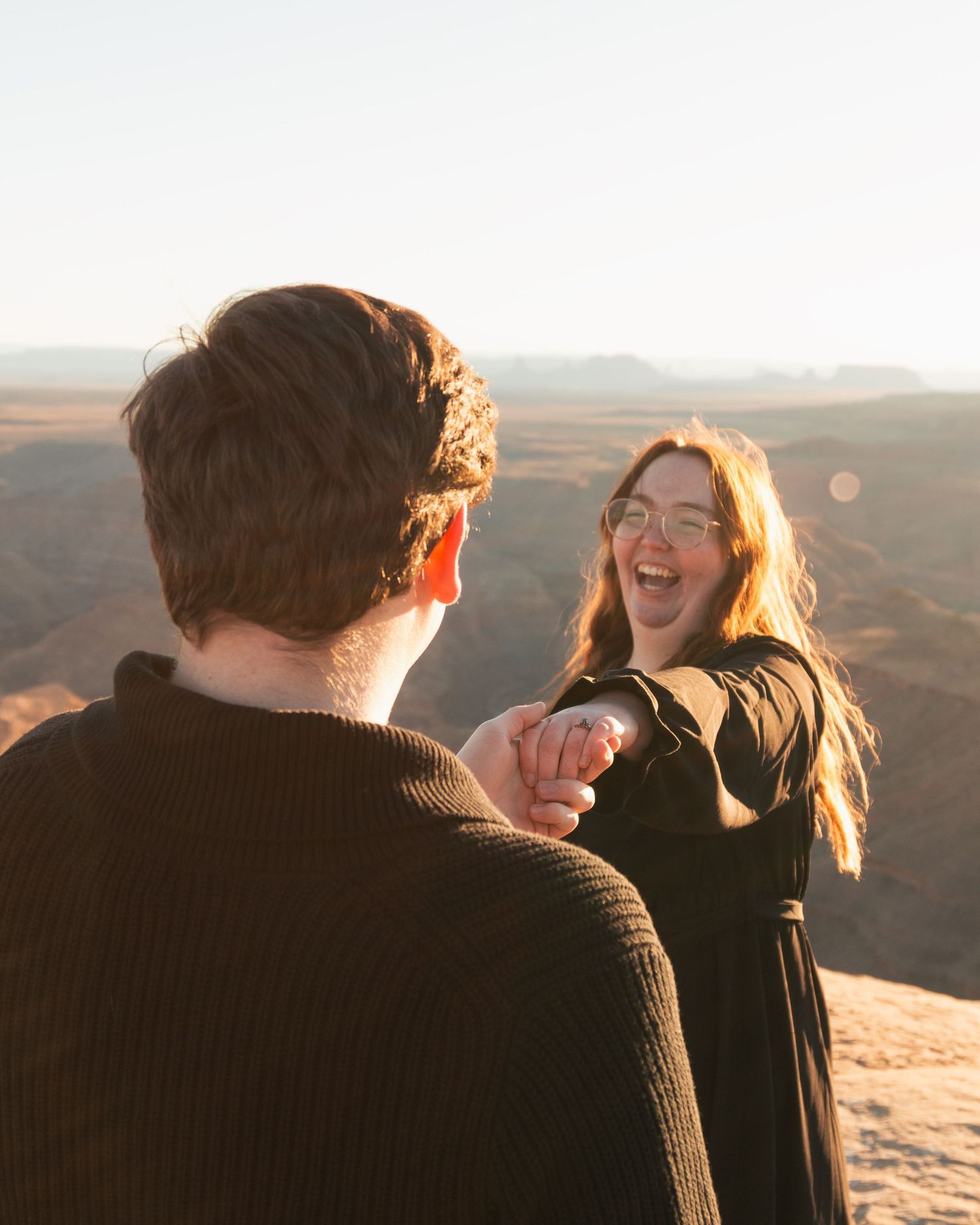 Couple sharing a joyful moment on desert cliff during golden hour.