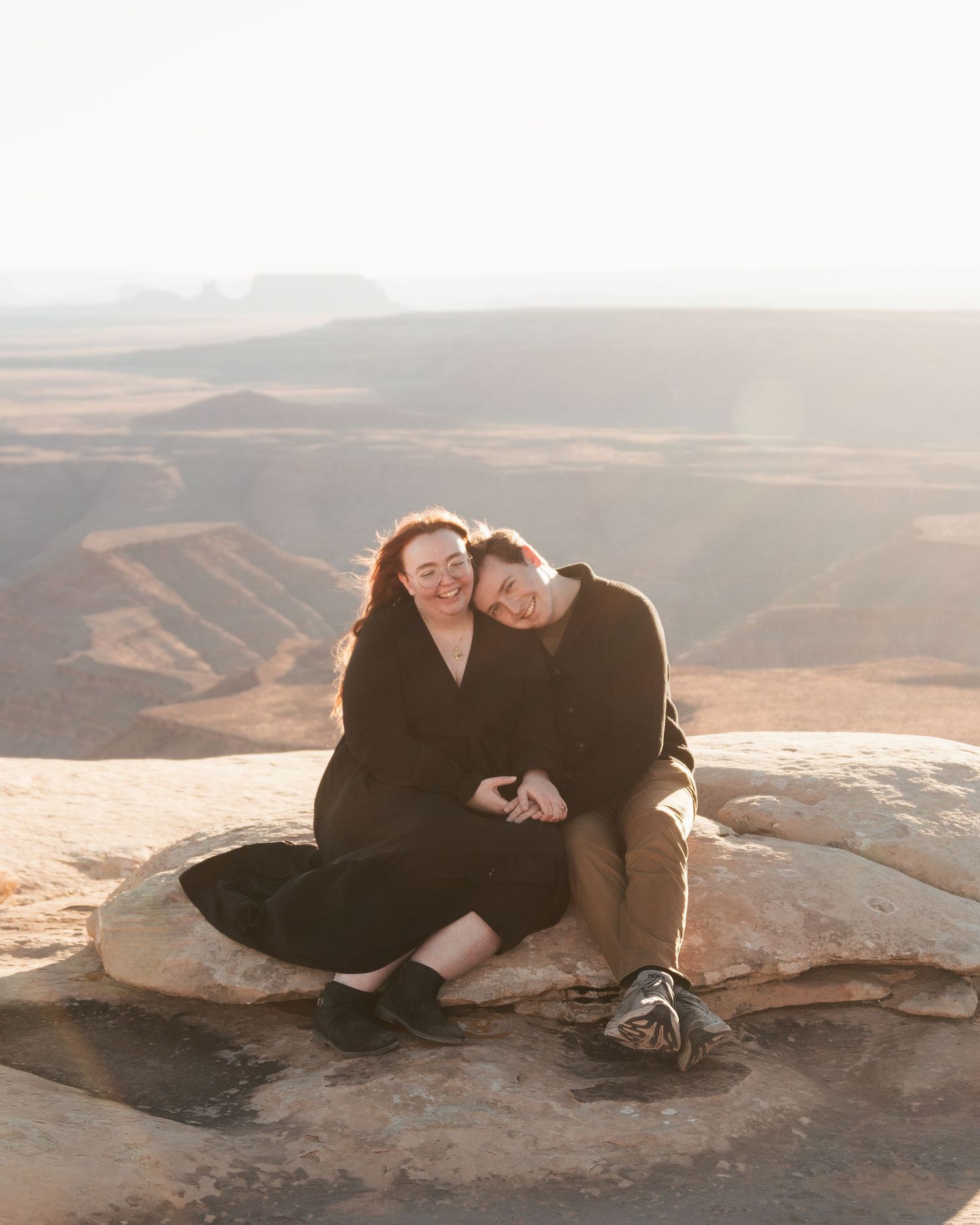 A couple lounges together on red rock formations in desert landscape.