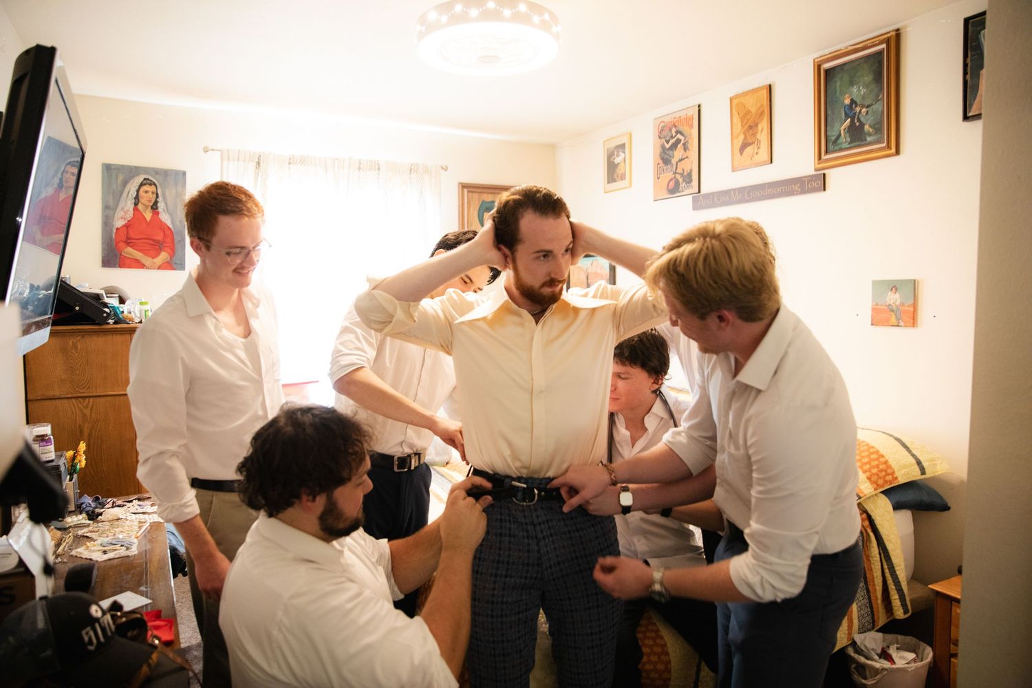 Group of people in white shirts gathered in a small room looking at something together.